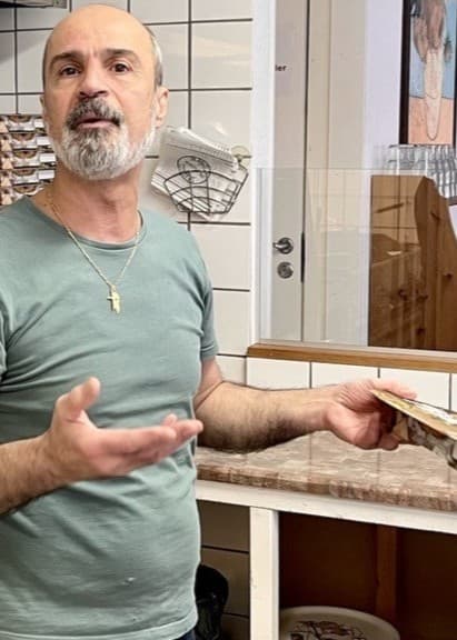 Pizzeriaägaren Elie Tohmi står i ett kök med pizzaugnar och visar en pizza medan han uttrycker kritik mot anonyma recensioner på nätet.