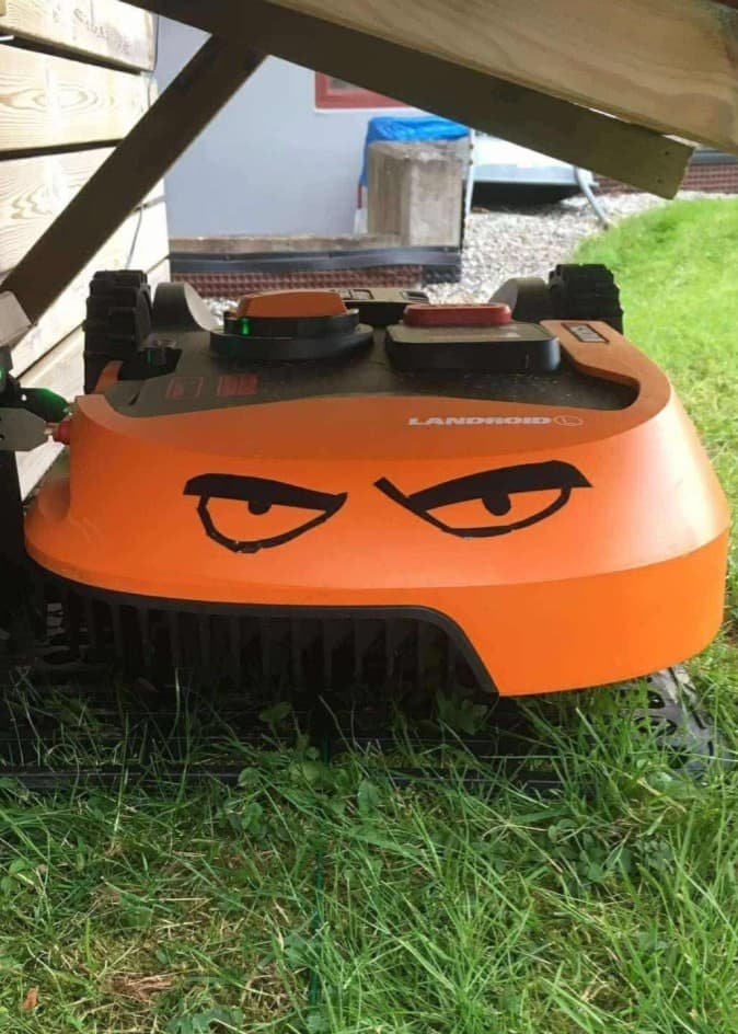 Robotgräsklipparen Gudrun som rymde från tomten ses på gräsmattan under en träkonstruktion.