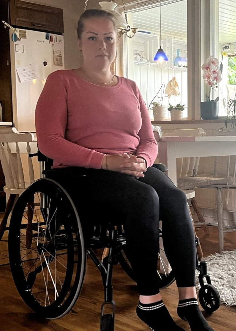 Angelica Henriksen sitter i rullstol i sitt kök efter en vårdskada. 