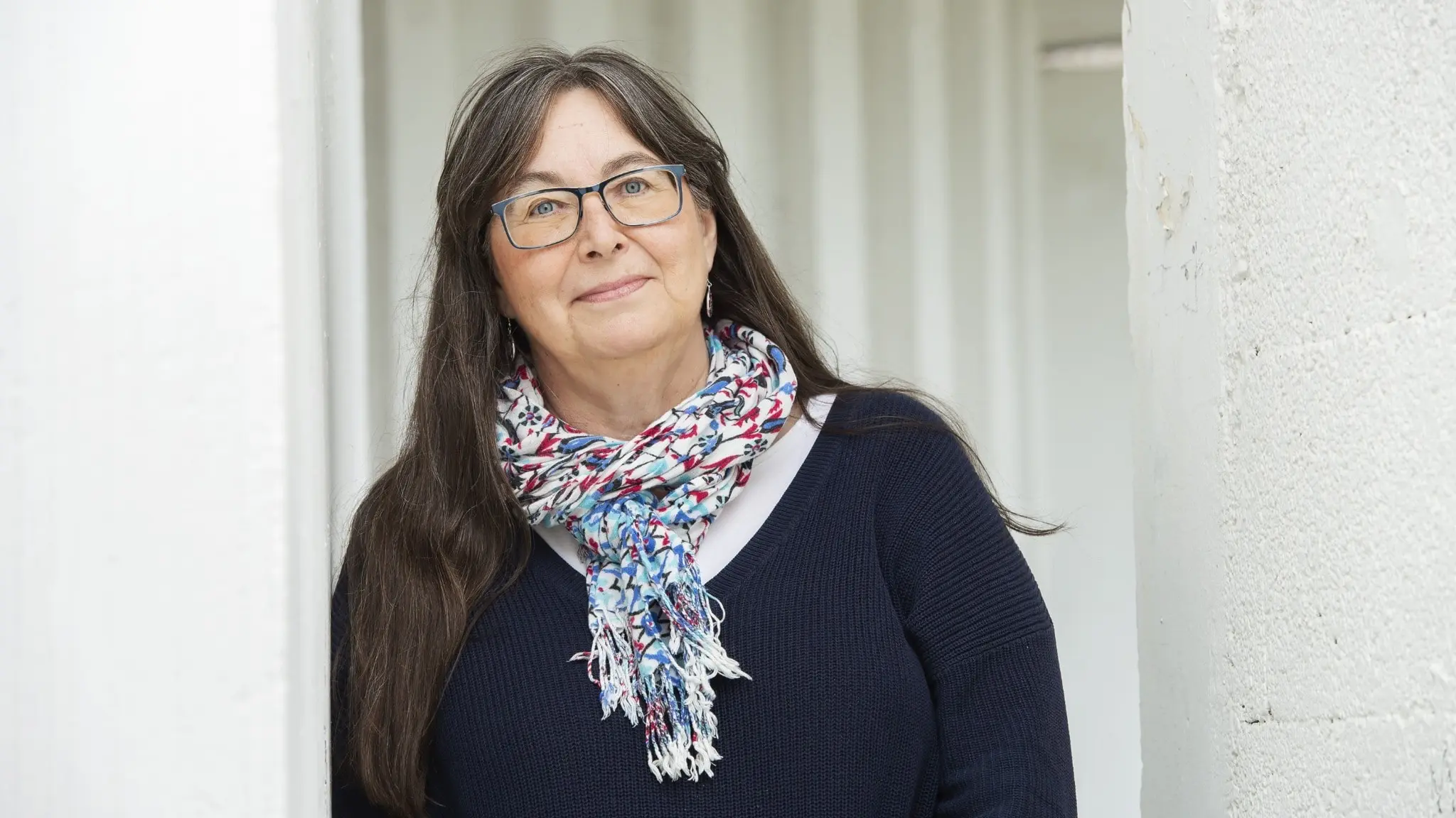 Kerstin Svensson, professor i socialt arbete vid Lunds Universitet, står utomhus vid en ljus vägg. Hon har mörkt hår, en mönstrad scarf och mörk tröja.