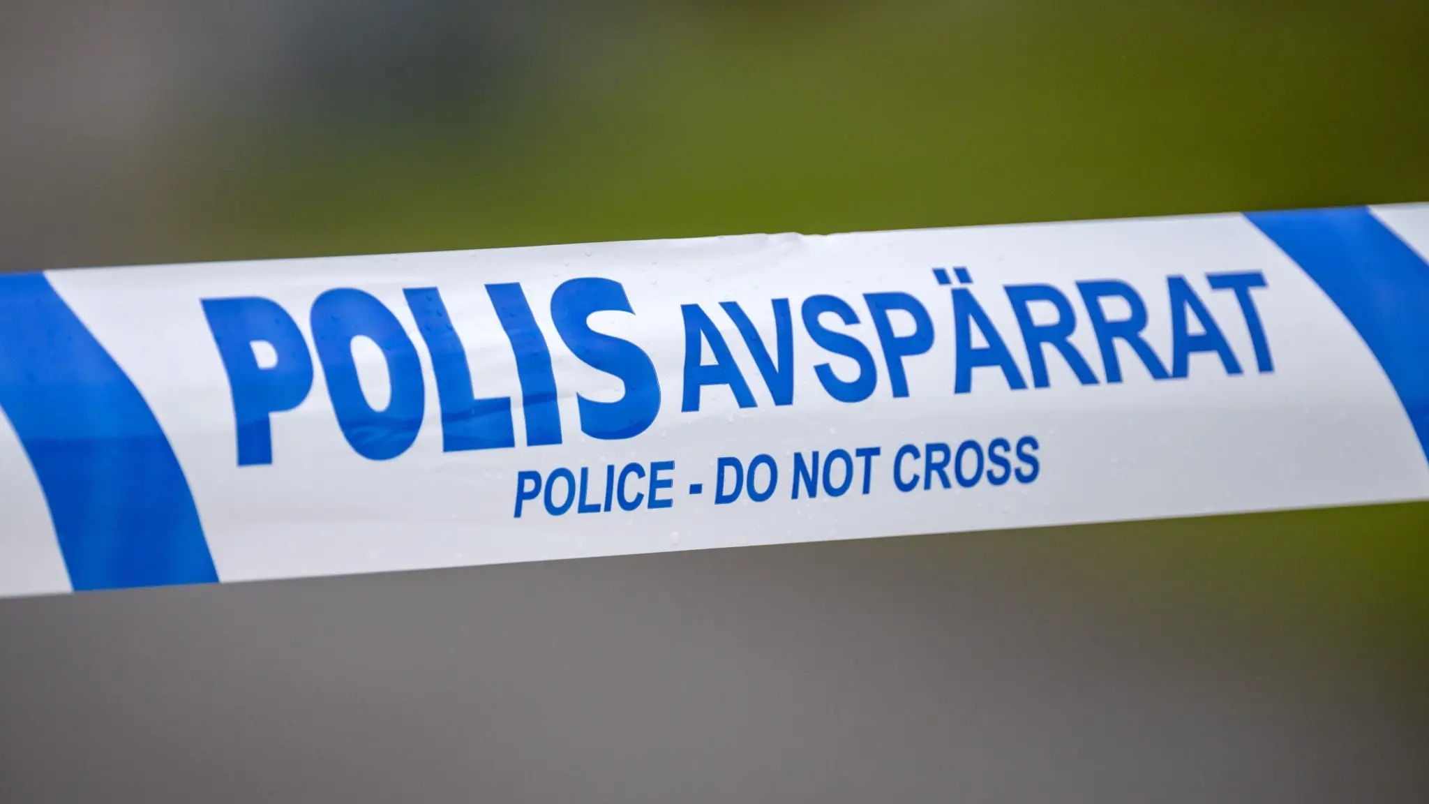 Närbild på ett blått och vitt polisavspärrningsband med texten 'POLIS AVSPÄRRAT' efter en explosion i Arlöv. Otydlig bakgrund med grönska.
