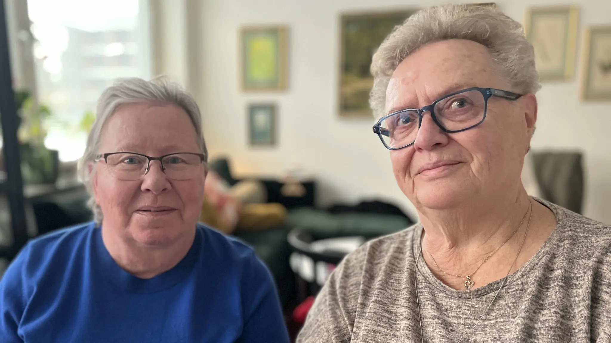 Två äldre kvinnor tittar in i kameran, båda har fyrkantiga glasögon och kort vitt hår. En har bå tröja och en har grå tröja, de sitter inomhus i en lägenhet. Köpstoppet i Huddinge. Mirjam Bäckman och Christina Jansén, PRO Huddinge.
