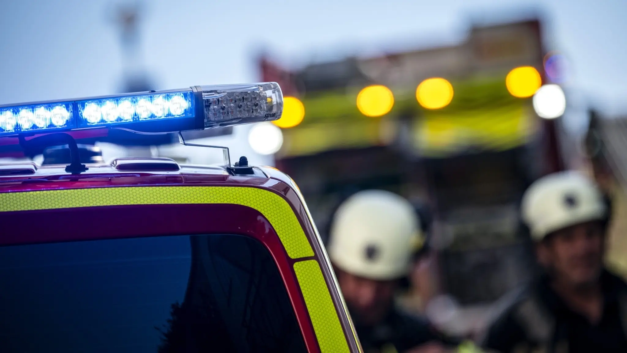 Brandmän i hjälmar står framför en brandbil med blinkande blåljus, fokus på fordonets ljusramp. Bilden förmedlar en känsla av akut insats och räddningstjänstaktivitet.