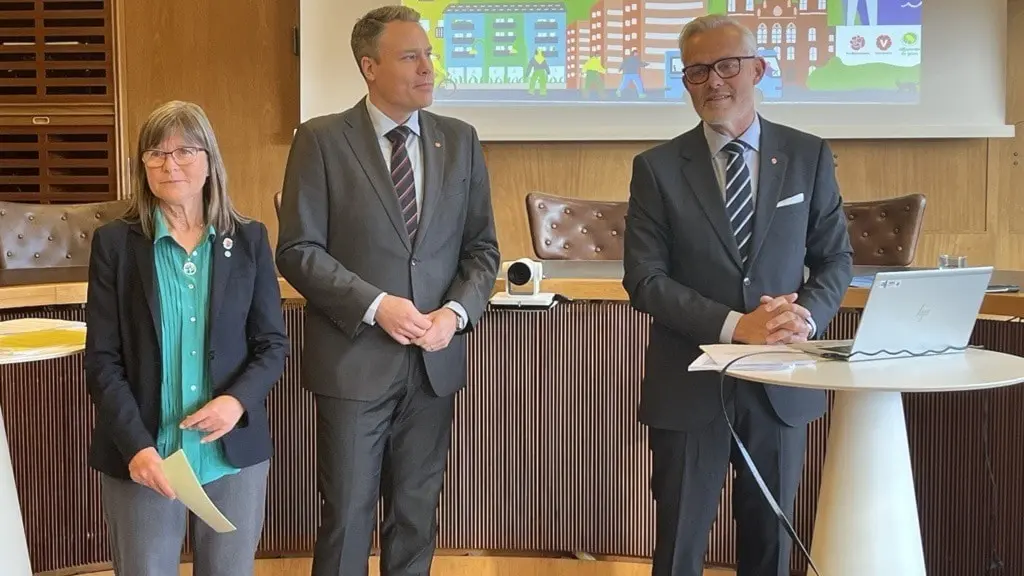 Karin Pleijel (MP), Daniel Bernmar (V) och Jonas Attenius (S) står framför en stor skärm med grafik som visar stadsplanering, under en pressträff i en konferenssal.