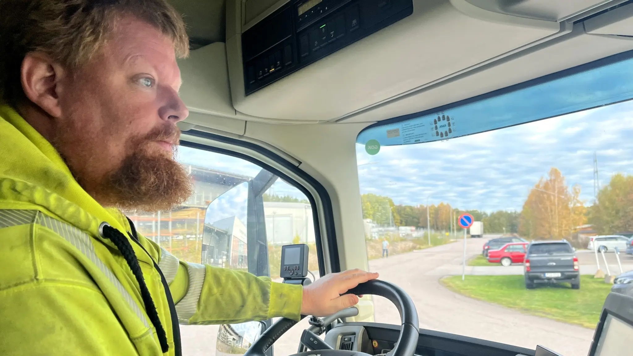En bild på en skäggig man från sidan som sitter i en förarhytt och håller i en ratt. 