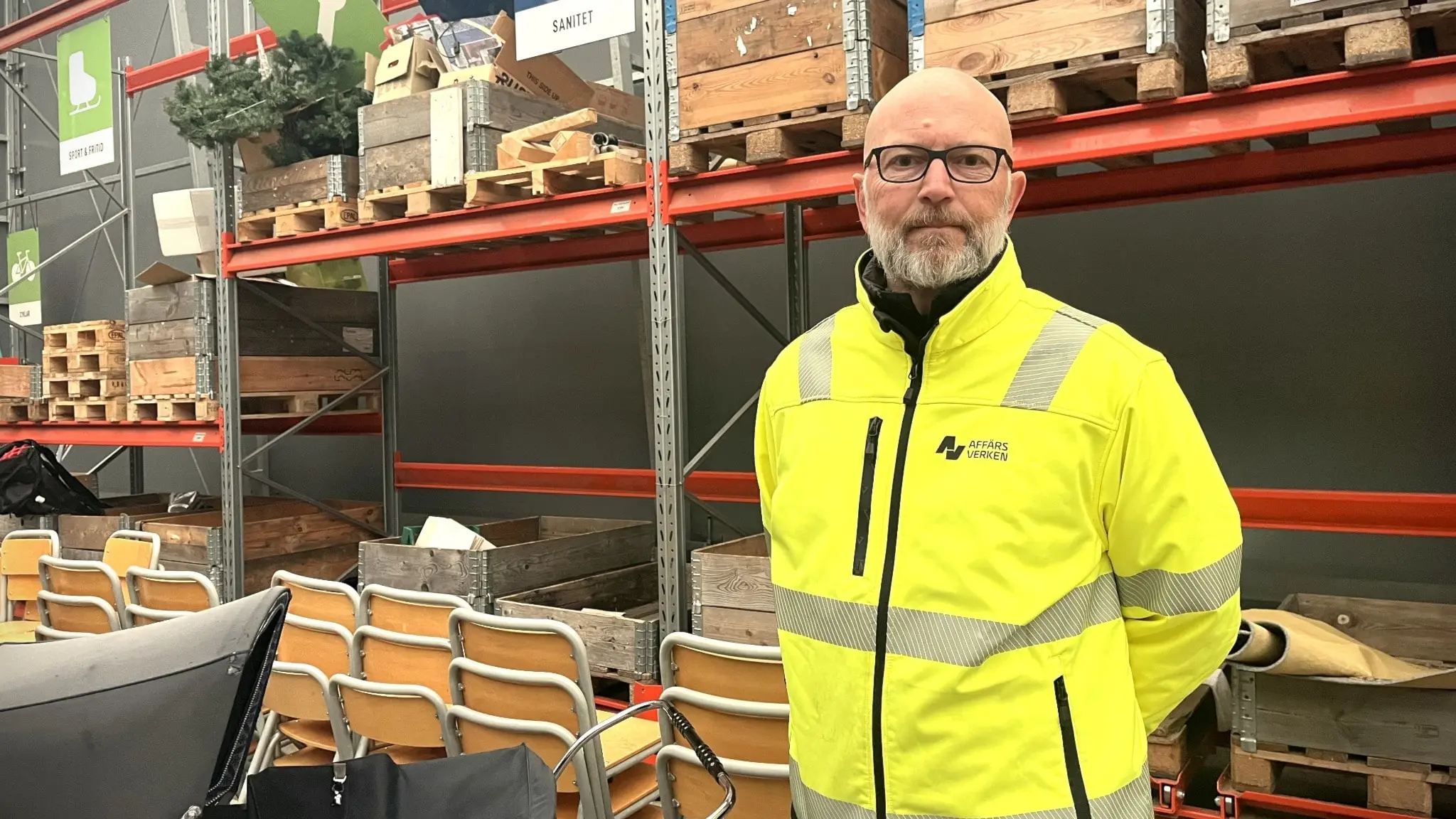 Robert Malmgren står på Mältans återvinningscentral. Han bär en gul varseljacka och är omgiven av återvinningsmaterial, inklusive träpallar och avlagda stolar på hyllor.