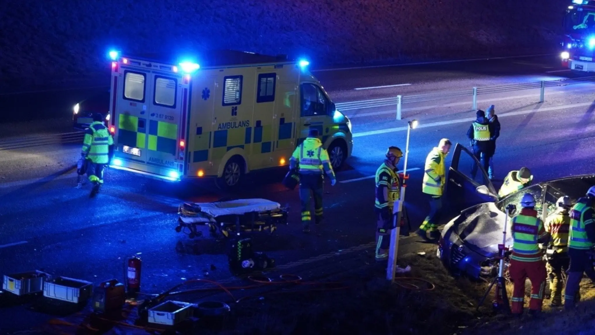 Ambulanspersonal och polis arbetar på en olycksplats under natten. En bil har blivit skadad i en trafikolycka, och en bår är framställd på vägen. Blåljus lyser upp området. Efter trafikolyckan – nu lämnar misstänkta politikern sina uppdrag
