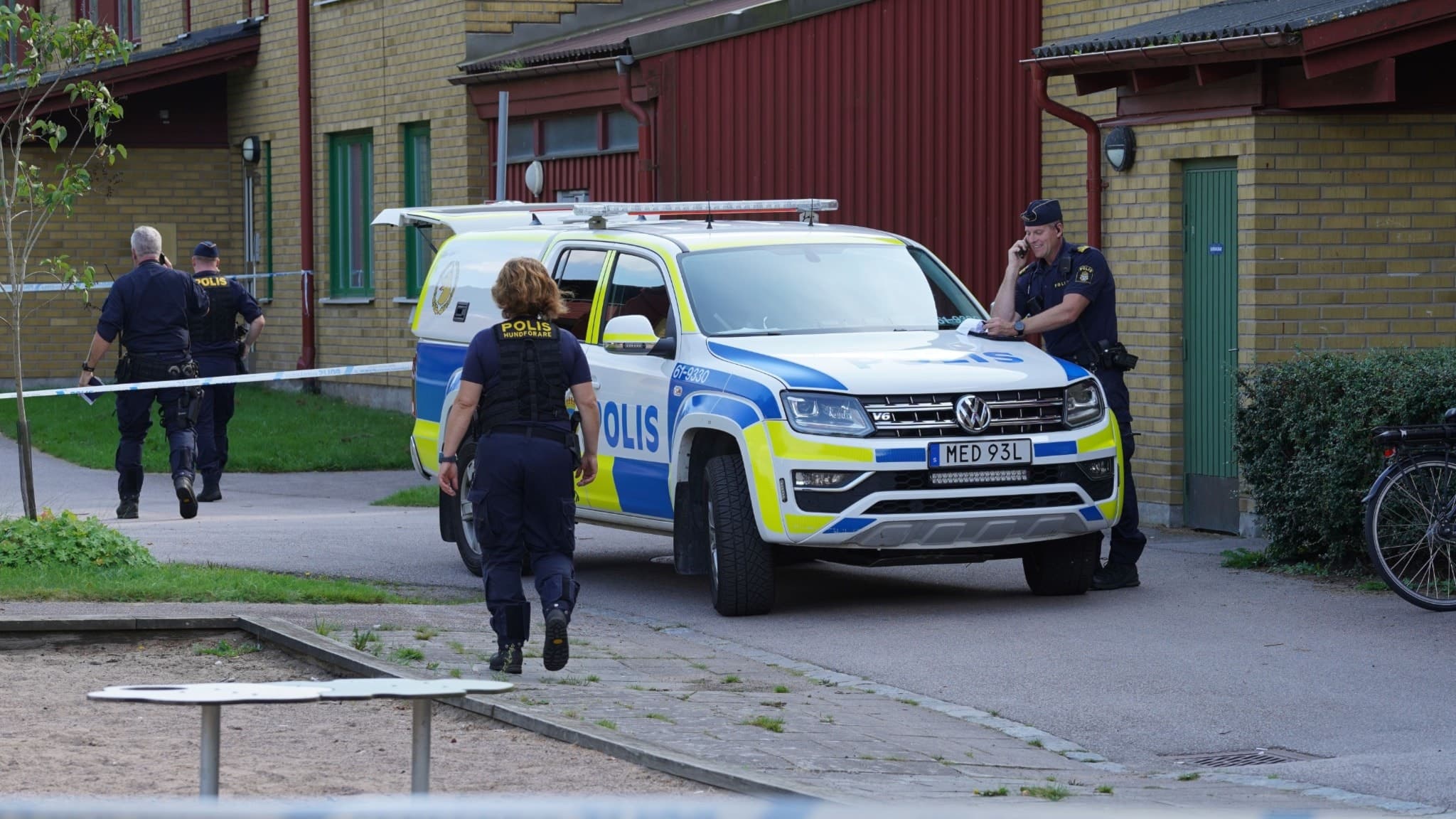 Polisinsats vid Teleborg med flera uniformerade poliser och en polisbil framför ett bostadsområde. Avspärrningar syns på platsen. 