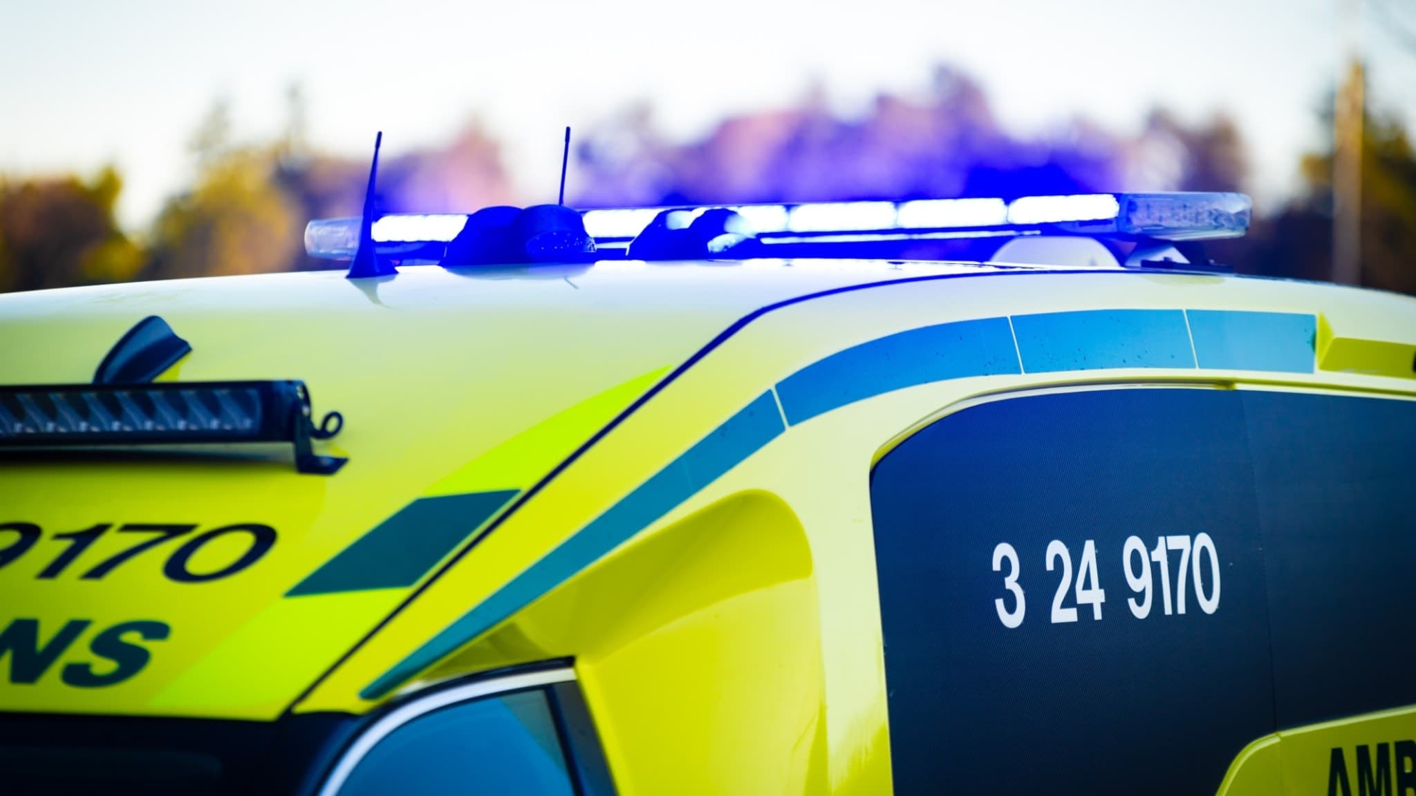 En gul ambulans med blåljus på taket står stilla utomhus.