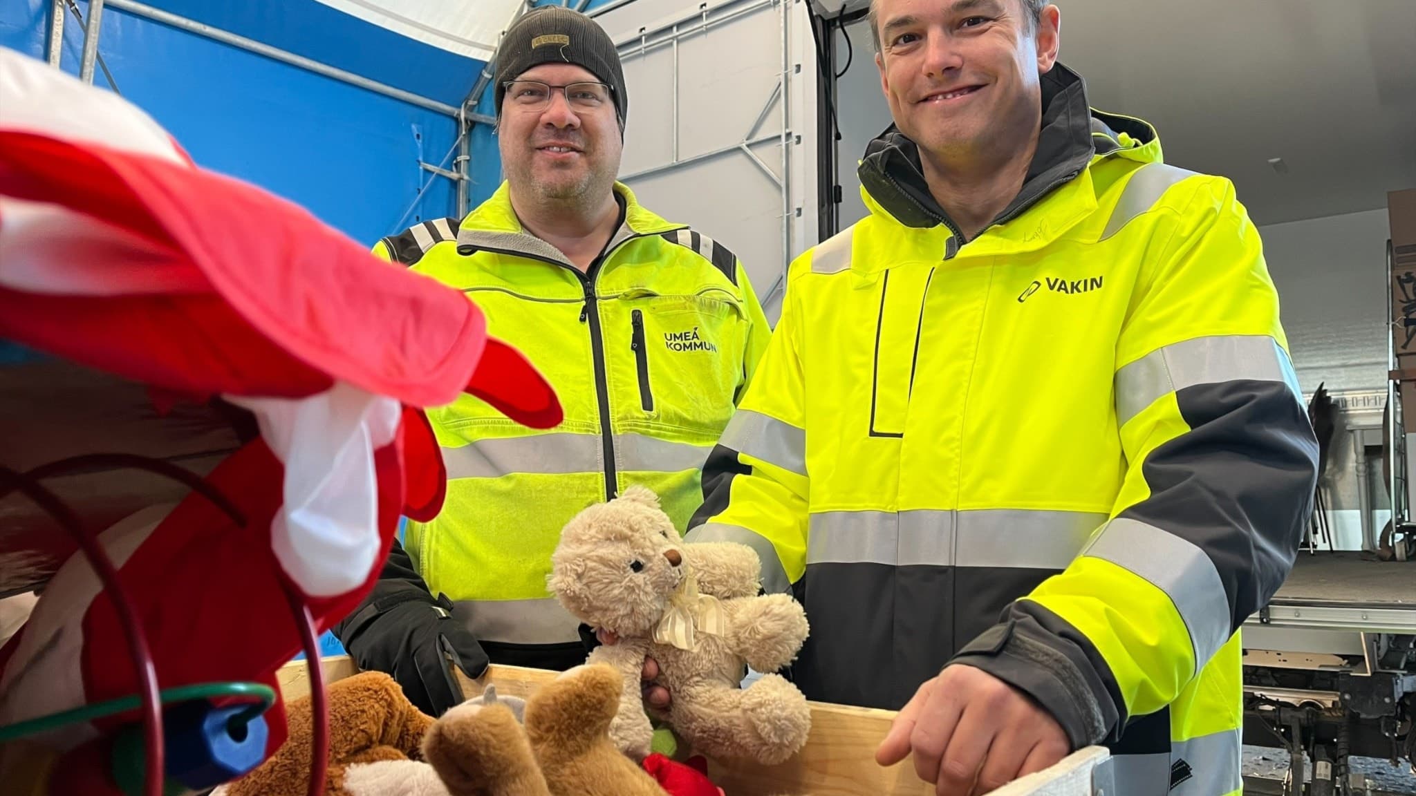 Två män i gula arbetsjackor, Oskar och Johnny Drotz, står vid Klockarbäckens återvinningscentral. Framför dem syns en låda med gosedjur som ska testas för återbruk.