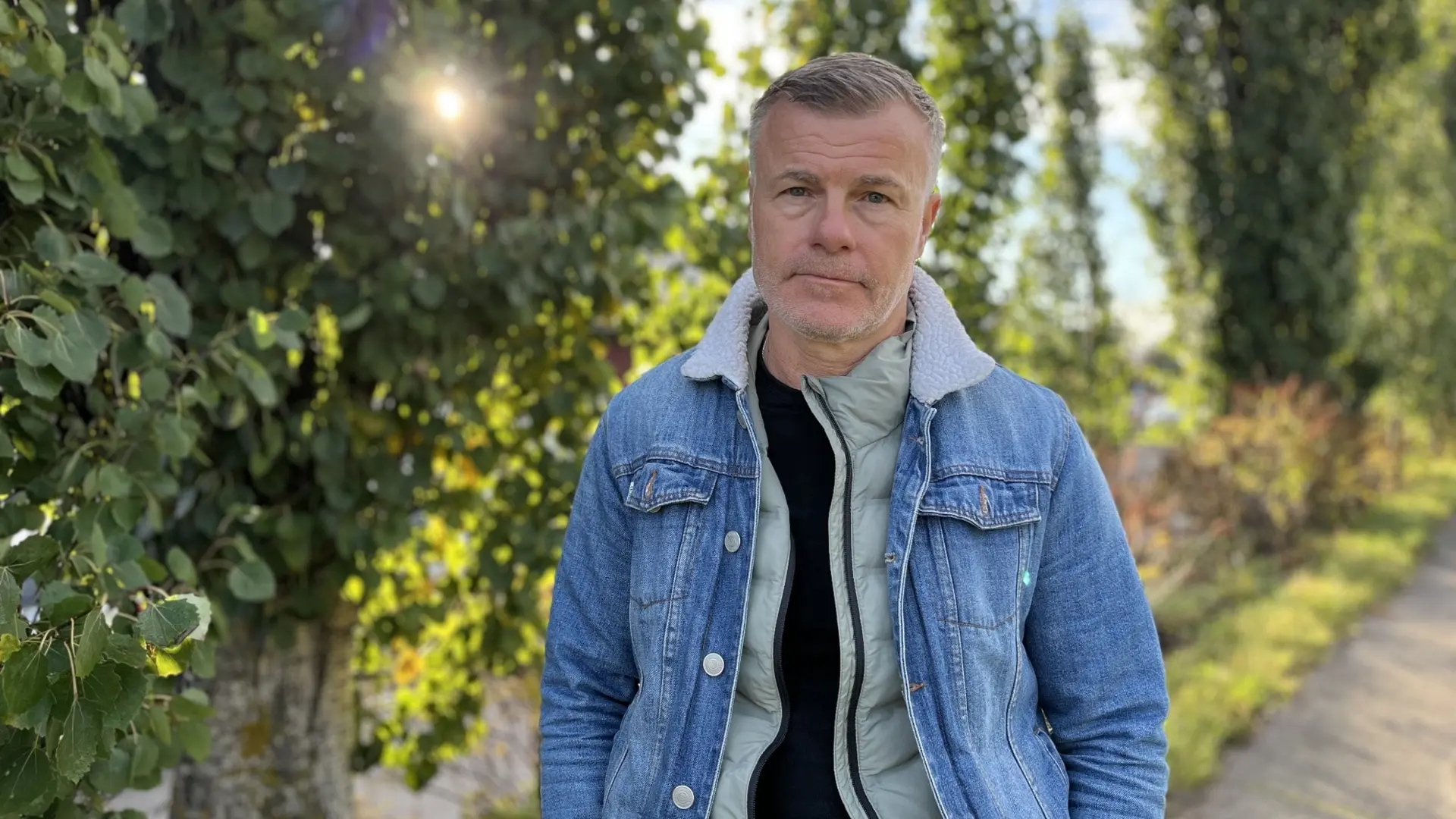 Regissören Gunnar Hall Jensen står i ett grönskande landskap i ljusblå jeansjacka.