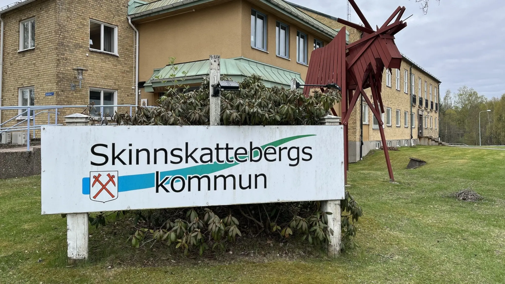 En skylt framför Skinnskattebergs kommunhus, det står ”Skinnskatteberg”. 