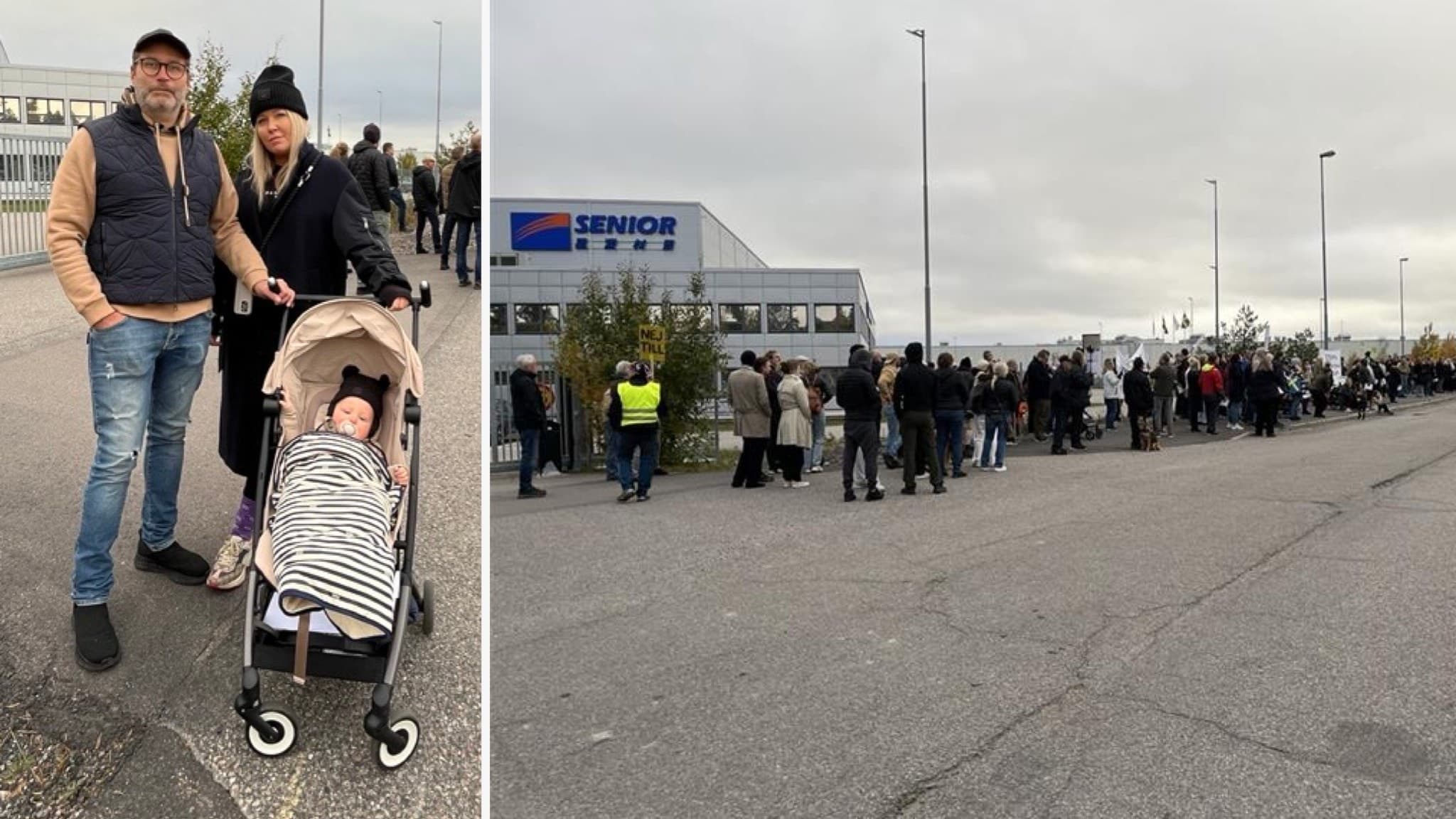Daniel Schelin och Martina Jansson står med barnvagn utanför Senior Materials i Eskilstuna. I bakgrunden syns en lång kö av människor vid fabriksområdet under en demonstration.