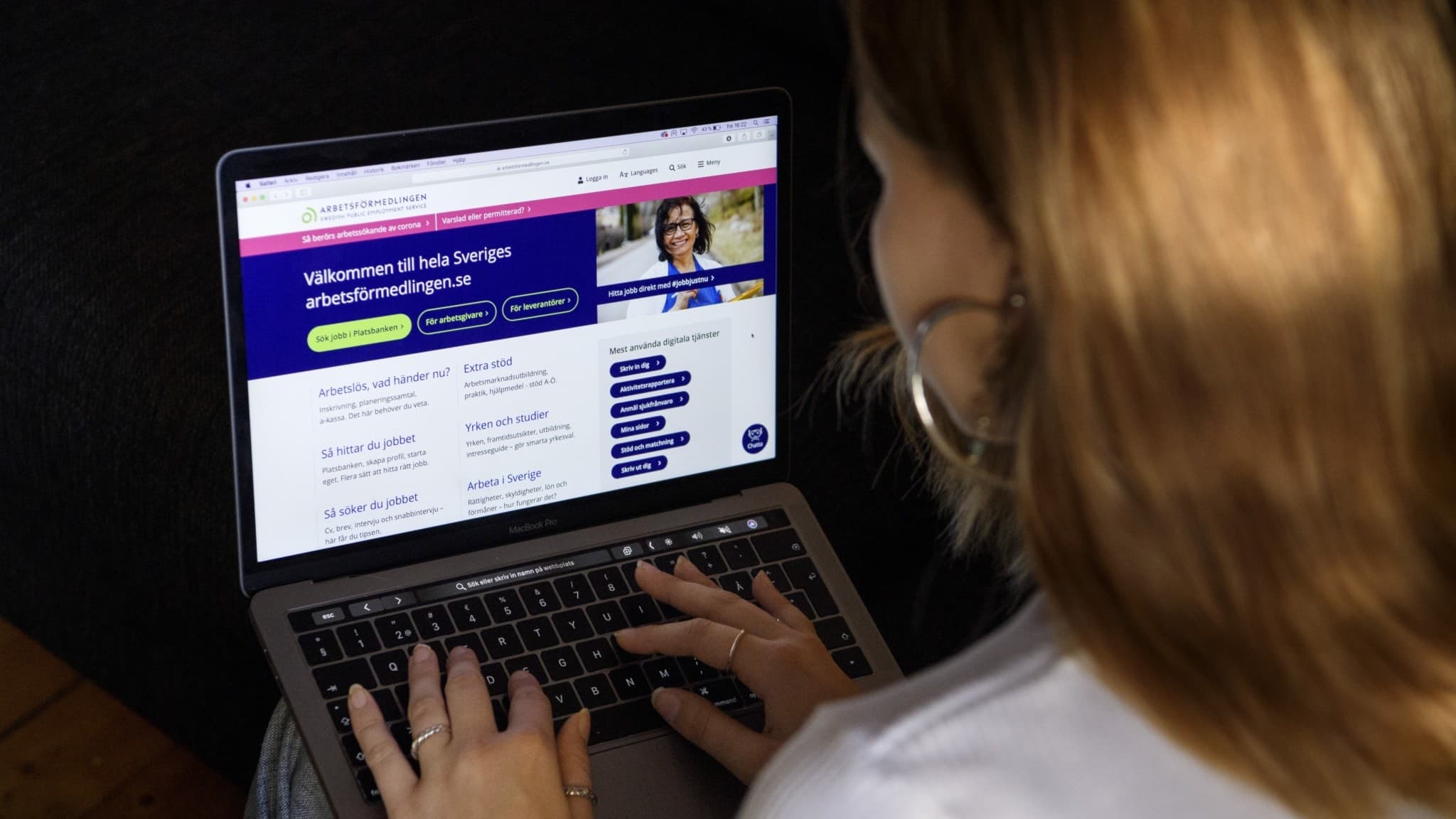 En ung kvinna sitter vid en laptop och navigerar på Arbetsförmedlingens hemsida, med fokus på att söka jobb. Skärmen visar rubriken 'Välkommen till din första arbetsförmedling'.