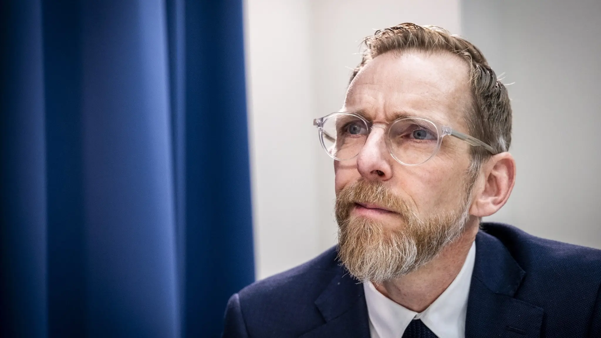Socialminister Jakob Forssmed (KD) i mörk kostym och slips talar framför en blå bakgrund.