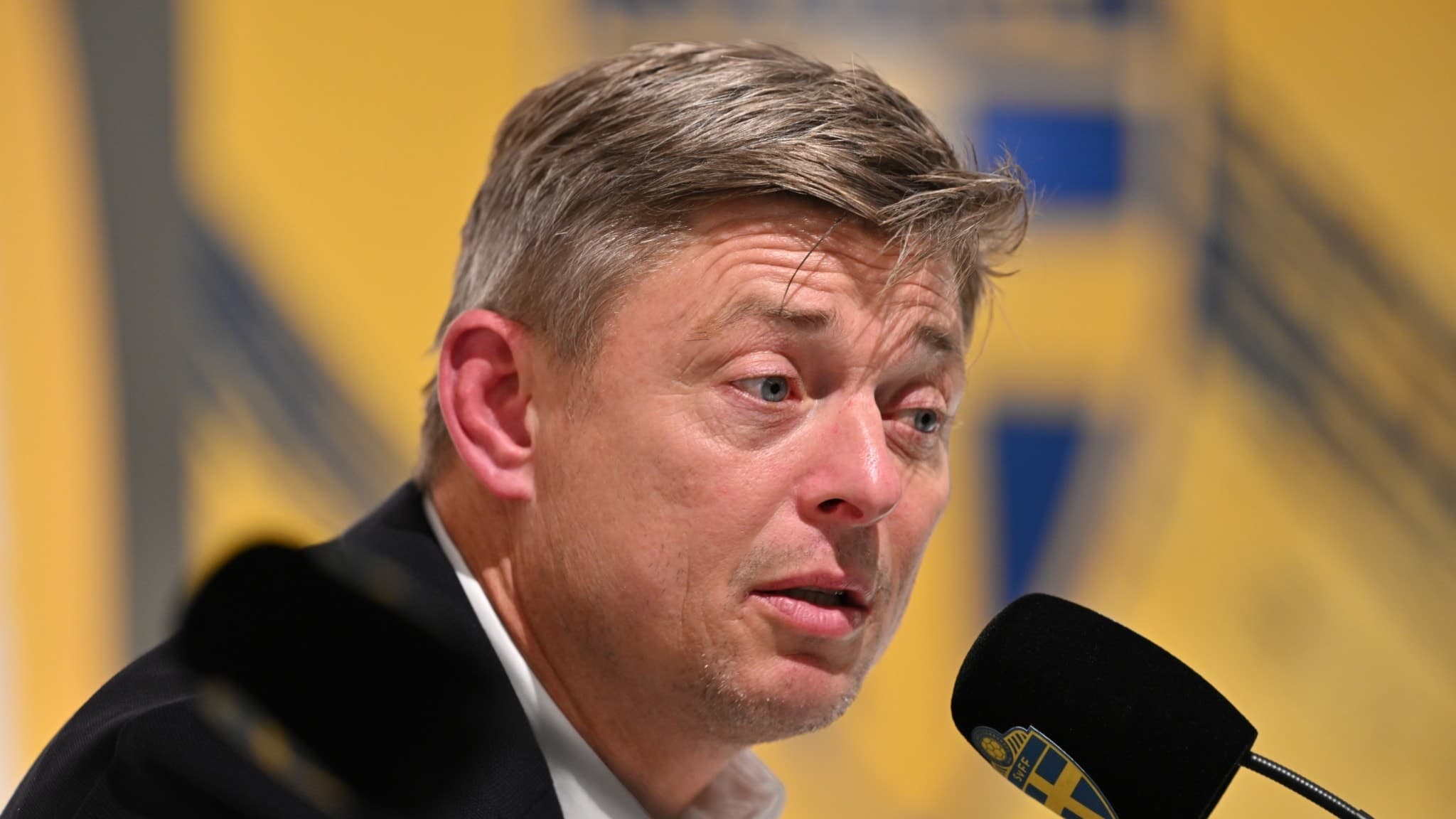 Sveriges förbundskapten Jon Dahl Tomasson ses vid en mikrofon under en presskonferens efter VM-kvalmatchen mellan Sverige och Kosovo på Ullevi, Göteborg. En svensk fotbollssymbol syns i bakgrunden.