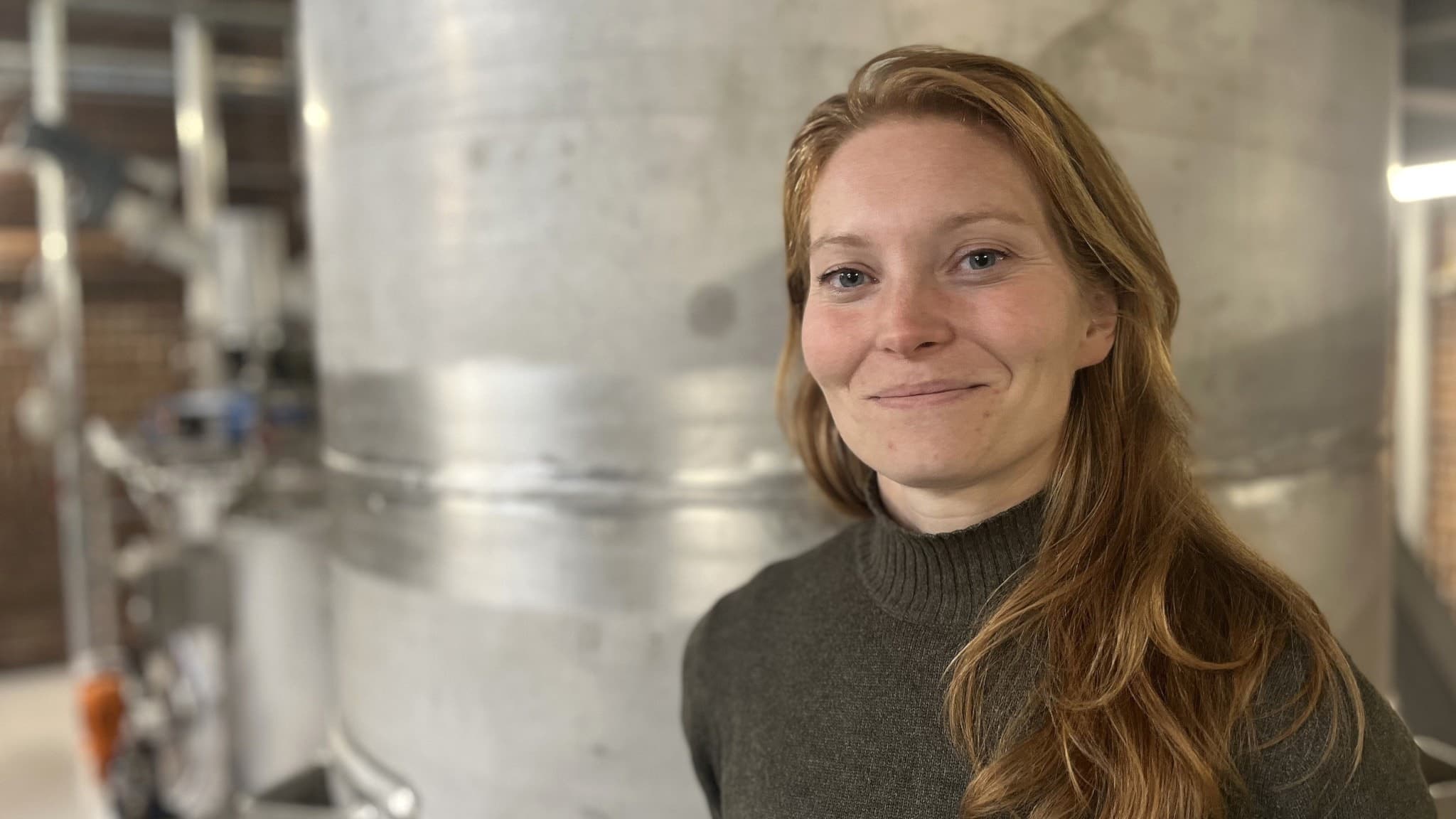 Emma Johansson, projektledare vid LBVA, står framför en stor metalltank i en industrimiljö med rör och tegelväggar i bakgrunden.