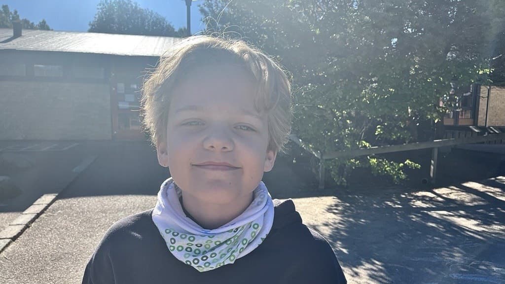 Linus Malm står utomhus i solljus framför en byggnad och grönska. Han bär en mörk tröja. Bilden är tagen i en ljus miljö med skuggor från träden.