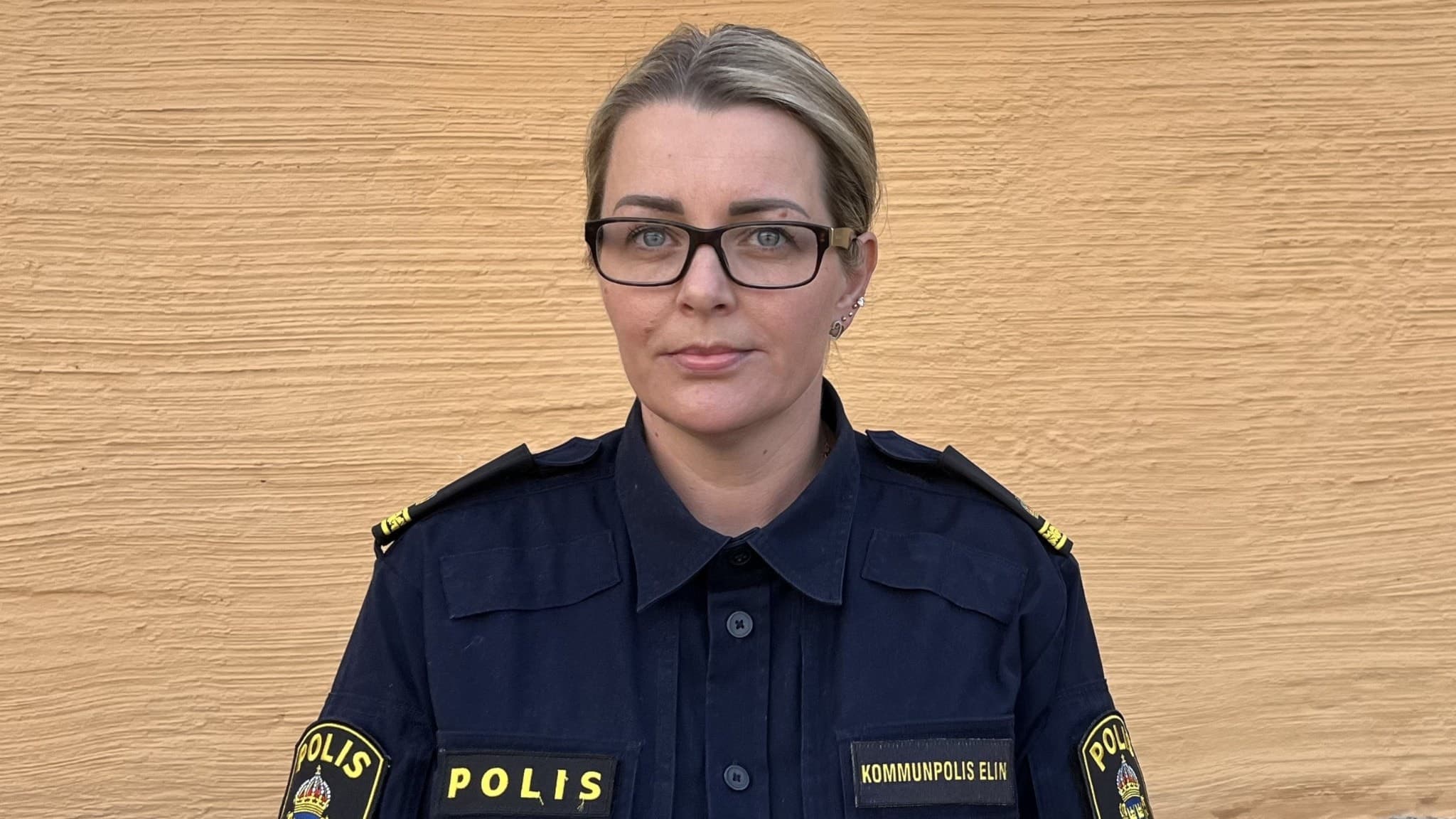 en kvinnlig polis som står framför en brunbeige bakgrund.