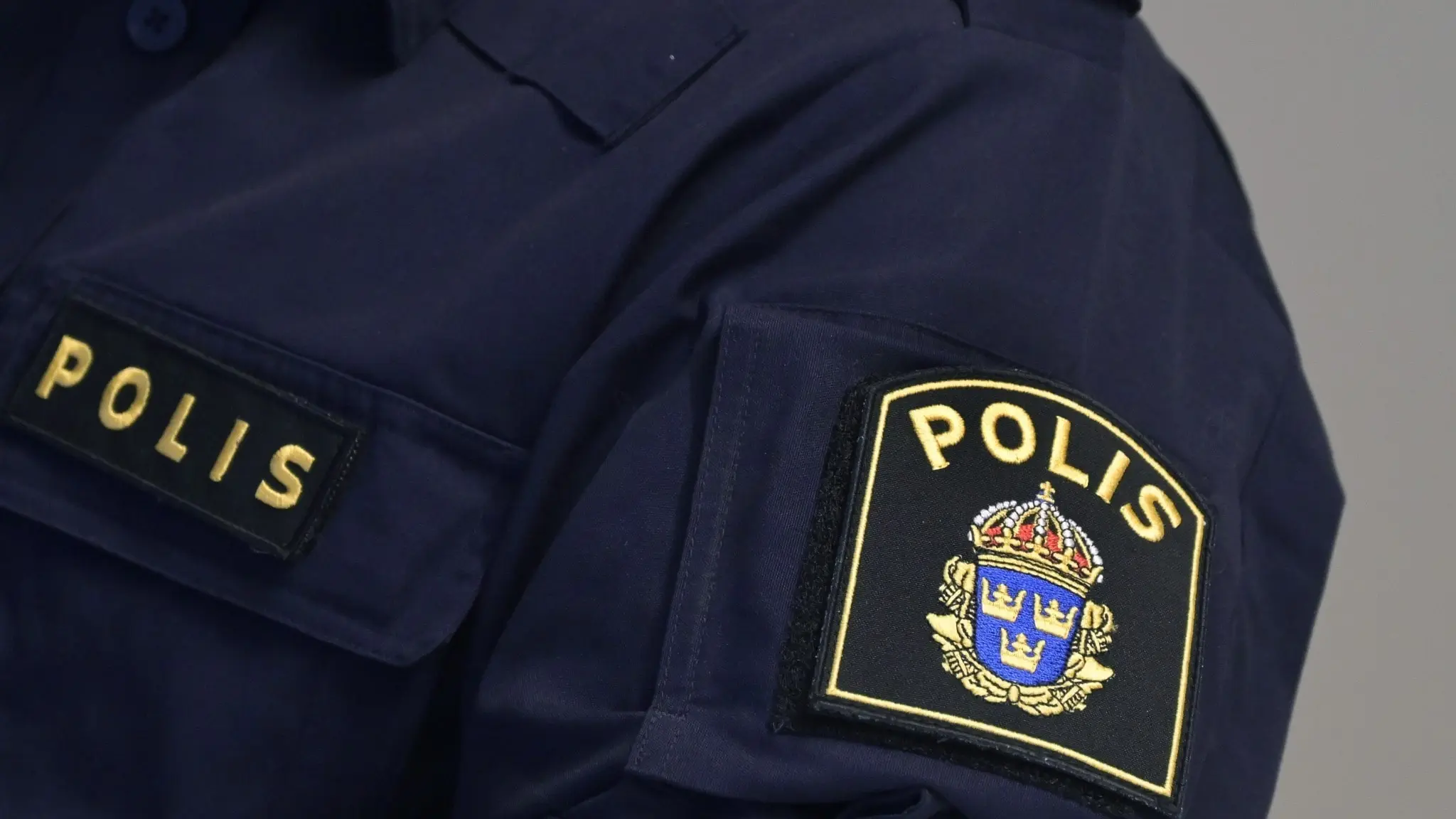 Närbild på en svensk polisuniform med texten 'POLIS' och polisens emblem på ärmen, vilket symboliserar rättsväsendet och trygghet.