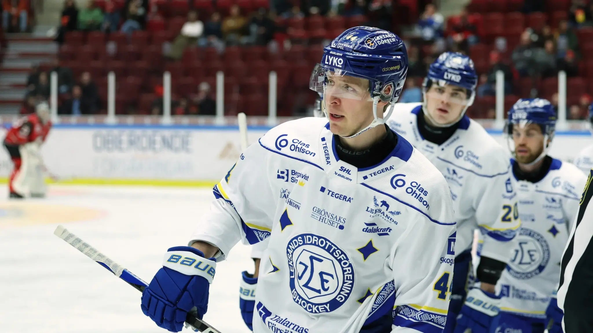 Tre hockeyspelare kommer på rad. De är klädda i blåvita hockeydräkter.