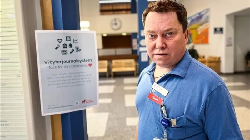 En man i blå arbetskläder står vid en informationsskylt om ett nytt journalsystem i en ljus och öppen reception. Skylten beskriver systemets funktioner med text och symboler