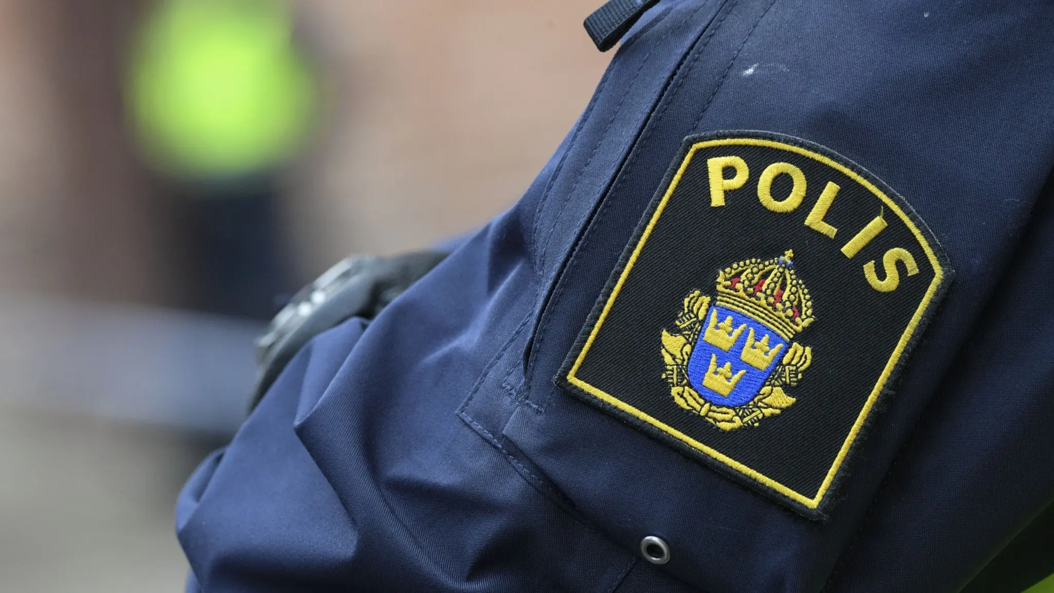 Närbild på en polisuniform med texten 'POLIS' och en svensk vapensköld.