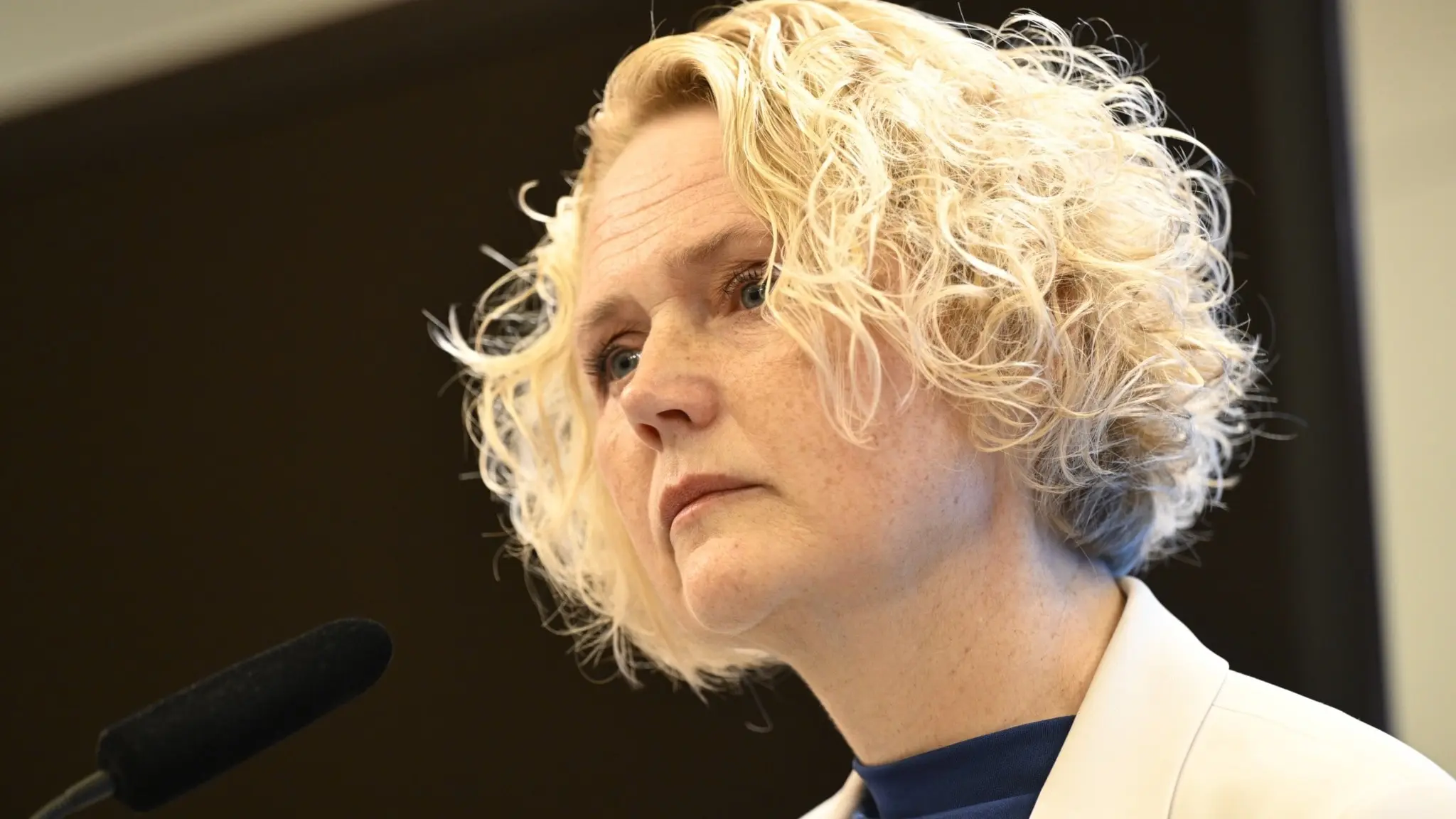 Centerpartiets partiledare Anna-Karin Hatt står vid en mikrofon under en pressträff i Stockholm där hon meddelar sin avgång. Hon är klädd i en ljus kavaj och har lockigt blont hår.