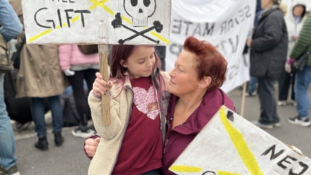 Anneli Reppe från Strängnäs deltar i en demonstration och håller skyltar med texten 'Nej till gift' och 'Nej till cancer' samt en dödskalle-symbol. Bakom henne syns flera personer med protestskyltar.