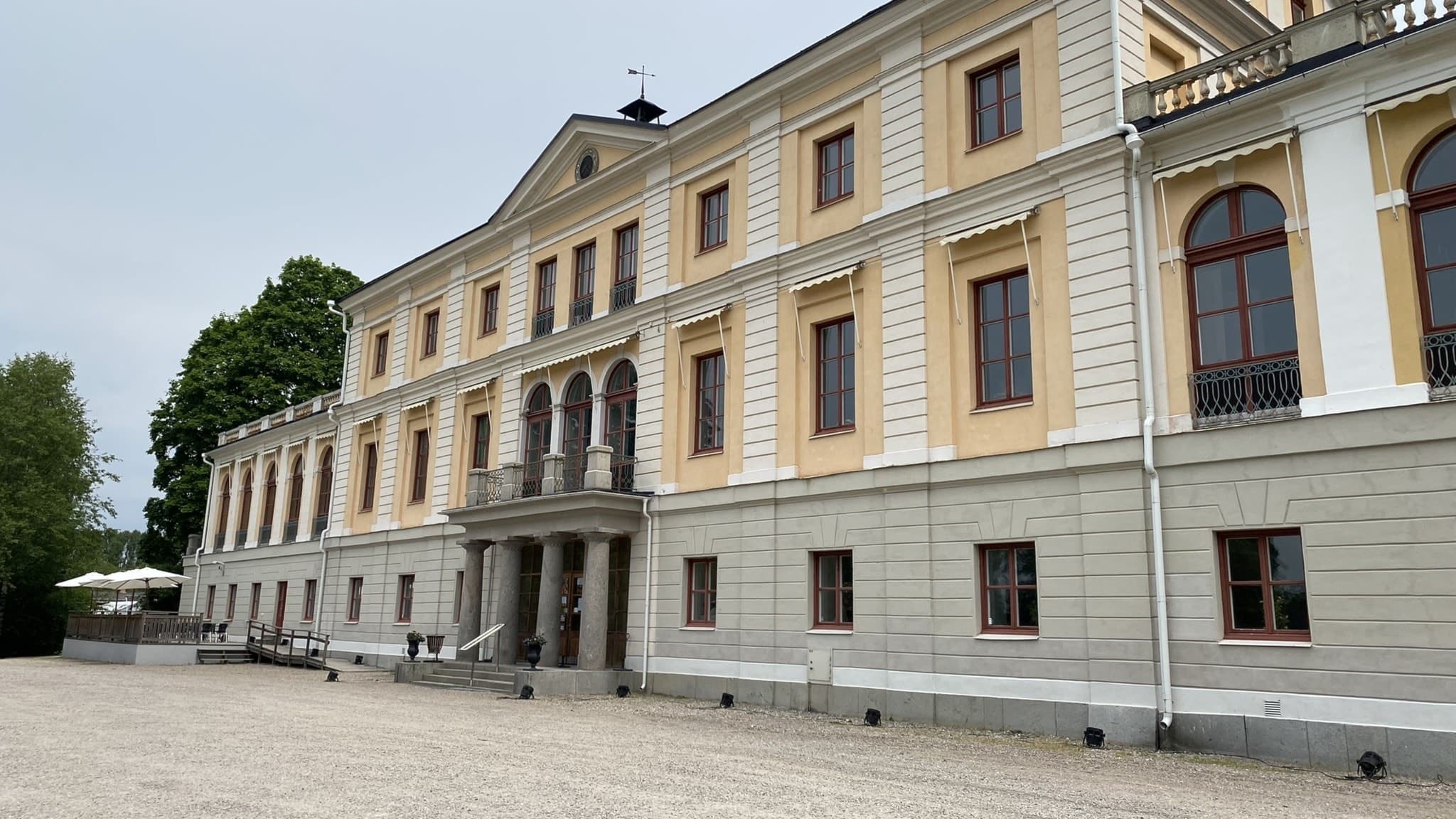 Säfstaholms slott i Vingåkers kommun, en ljusgul byggnad med klassisk arkitektur och stora fönster, omgiven av grönska och grusgångar.