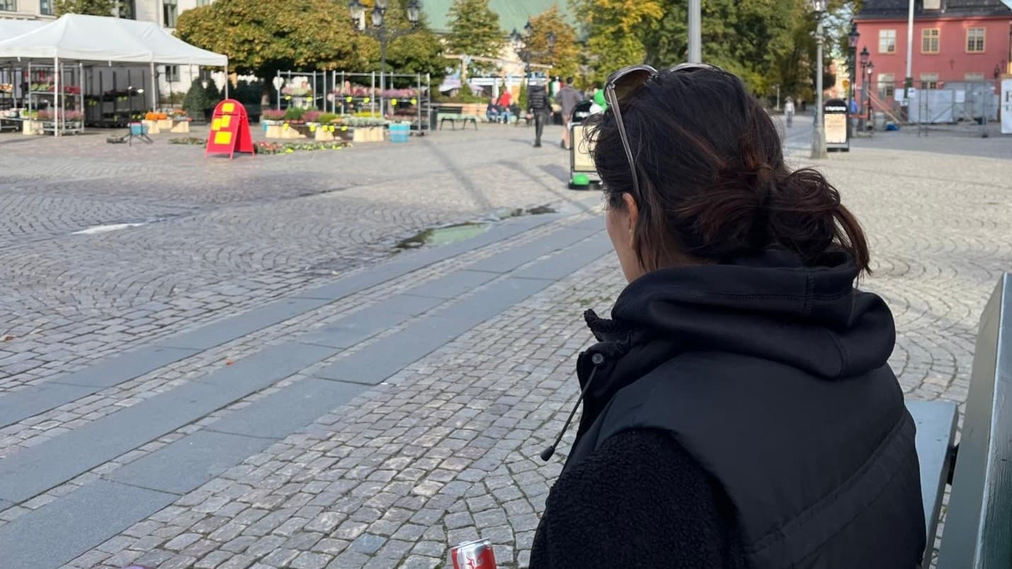 Tonårsmamman Doris ses bakifrån när hon nattvandrar ensam på ett stenlagt torg för att skapa trygghet för ungdomar. Hon bär mörka kläder och håller en dryck i handen.
