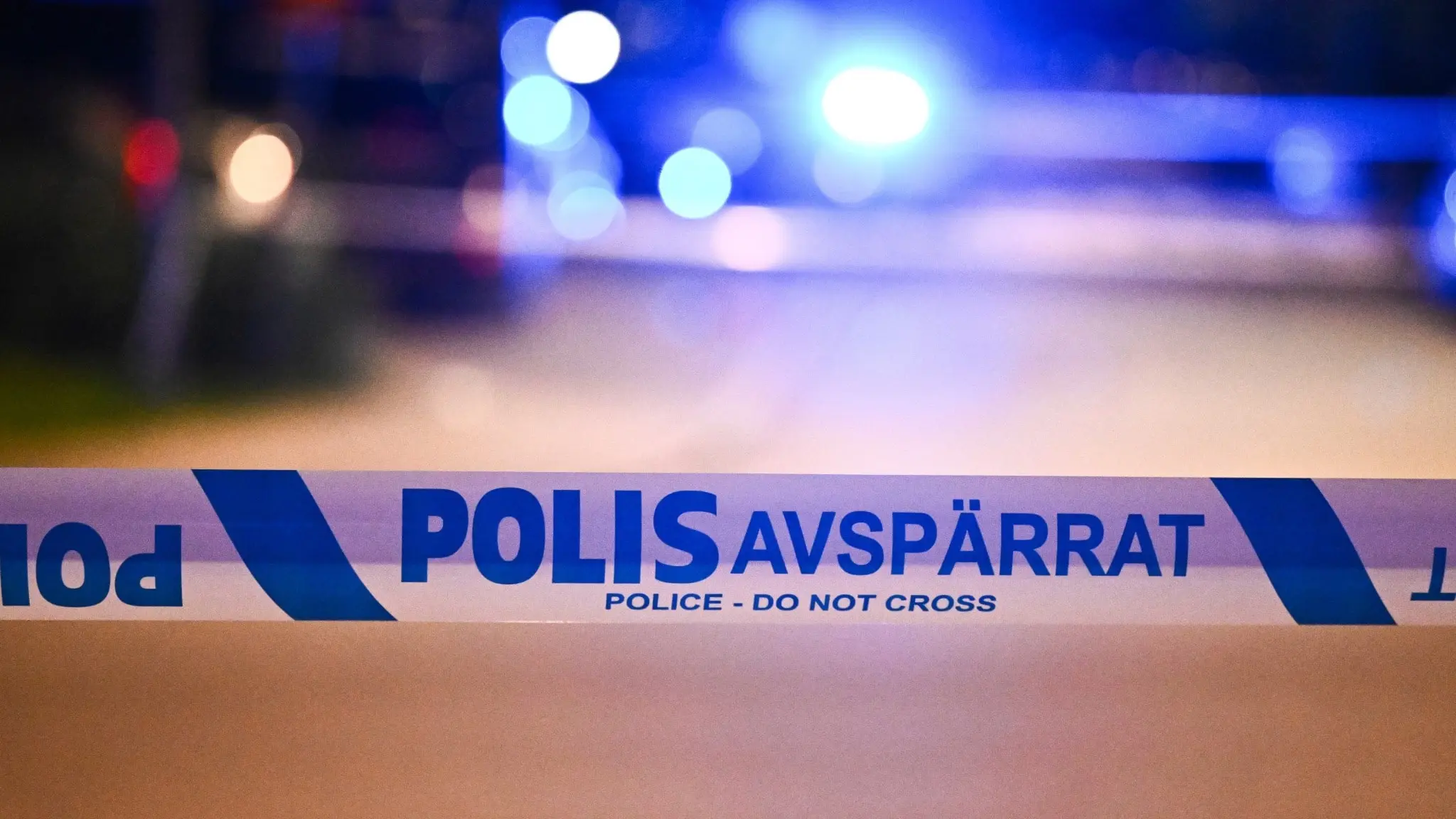 Polisavspärrningar på en gata i Hagsätra, Stockholm, efter en dödsskjutning. Blåljus från utryckningsfordon syns i bakgrunden.