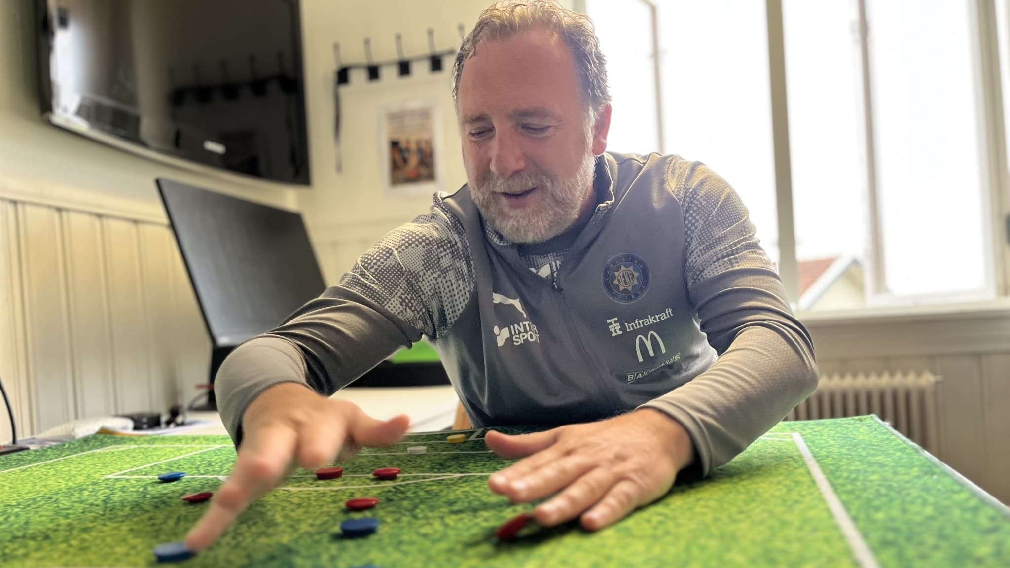 Albert Bunjaki, akademichef i Karlstad Fotboll och tidigare förbundskapten för Kosovo, gestikulerar över en taktiktavla med fotbollsplan och spelpjäser i ett mötesrum.