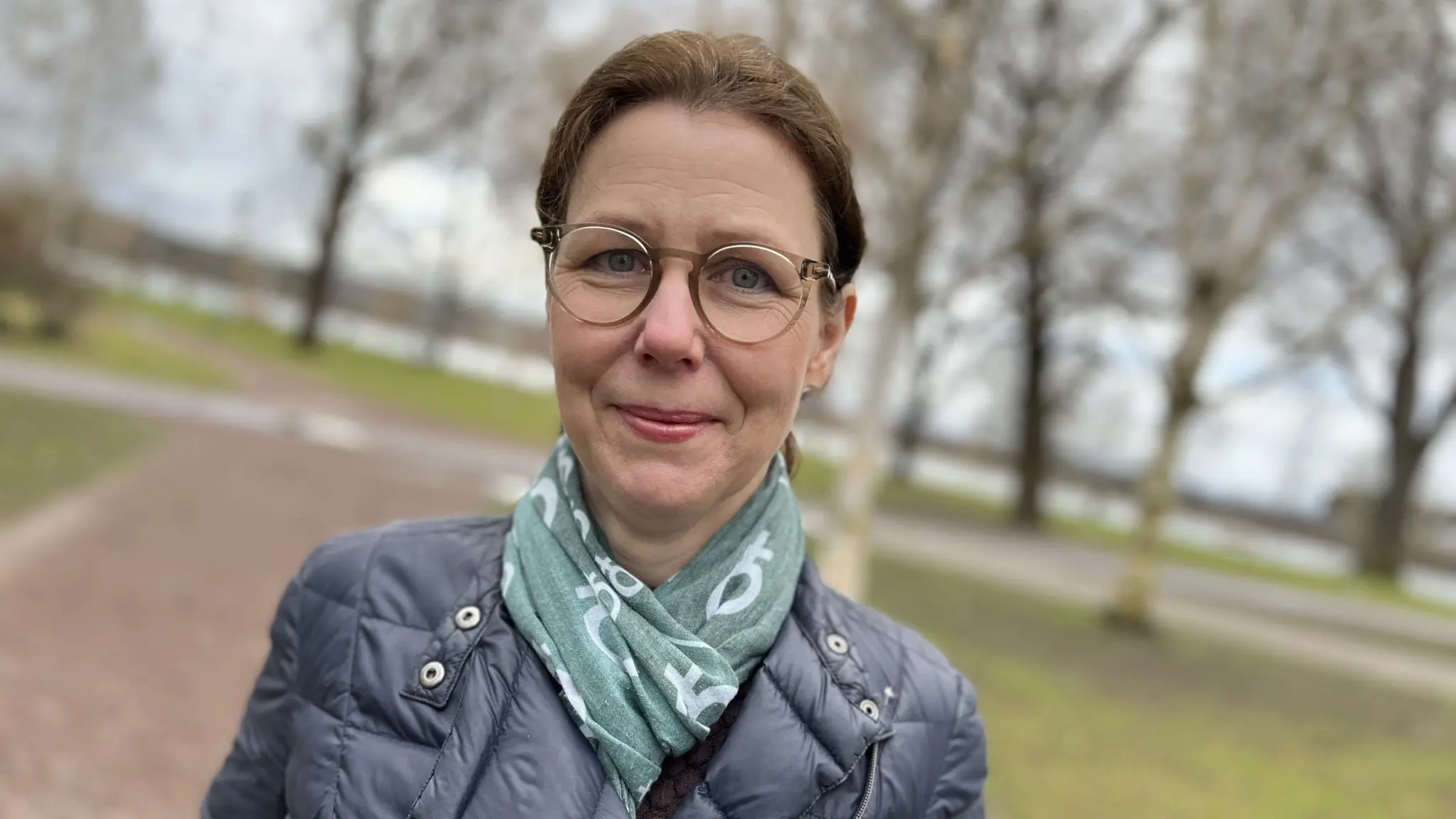 Mona Smedman (C), ersättare på Värmlandsbänken i Riksdagen, står utomhus i en park med träd i bakgrunden. Hon är klädd i en blå jacka och har en ljusblå halsduk runt halsen.