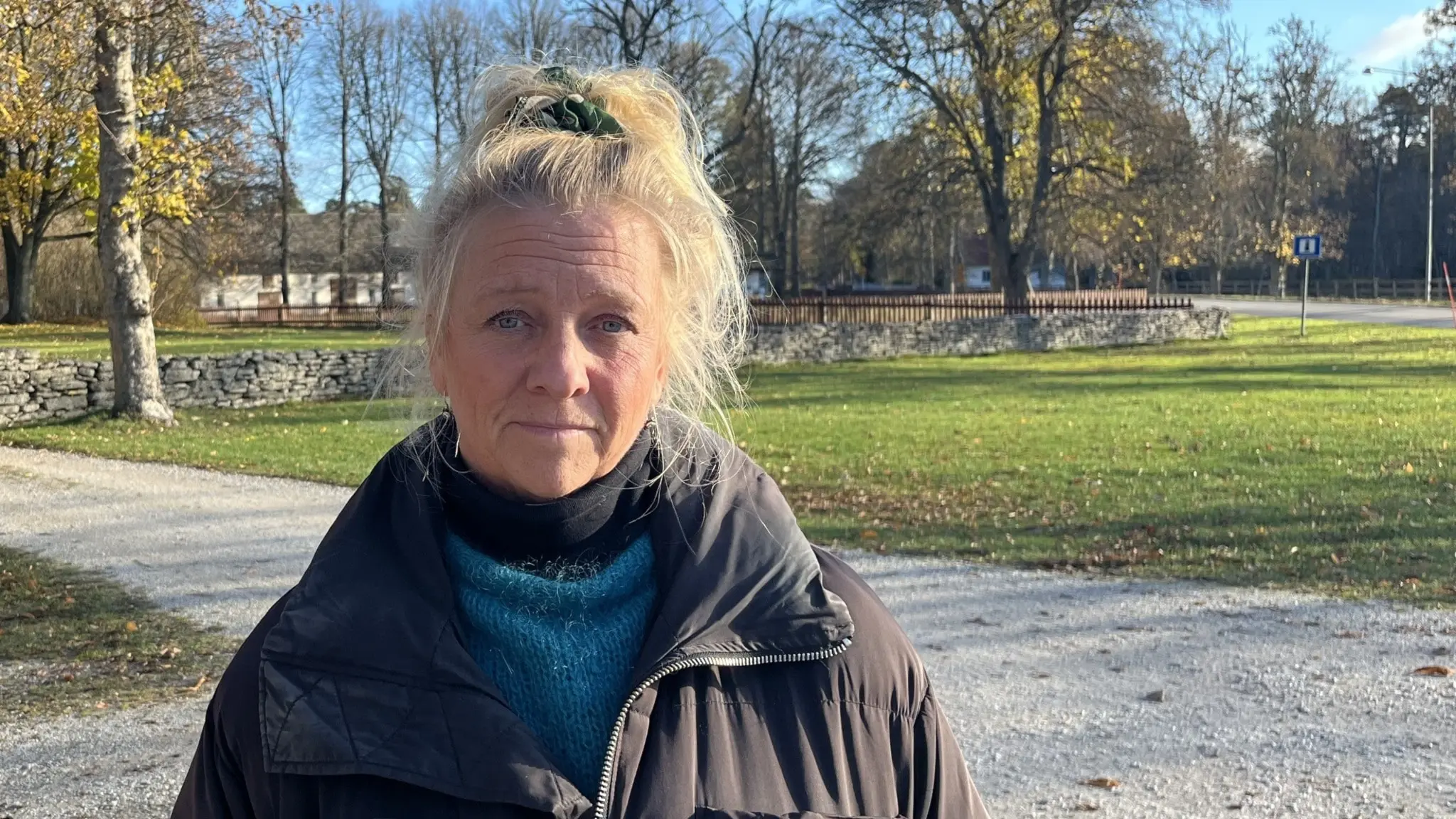 En kvinna med svart jacka står framför en grusväg och i bakgrunden syns några träd. 