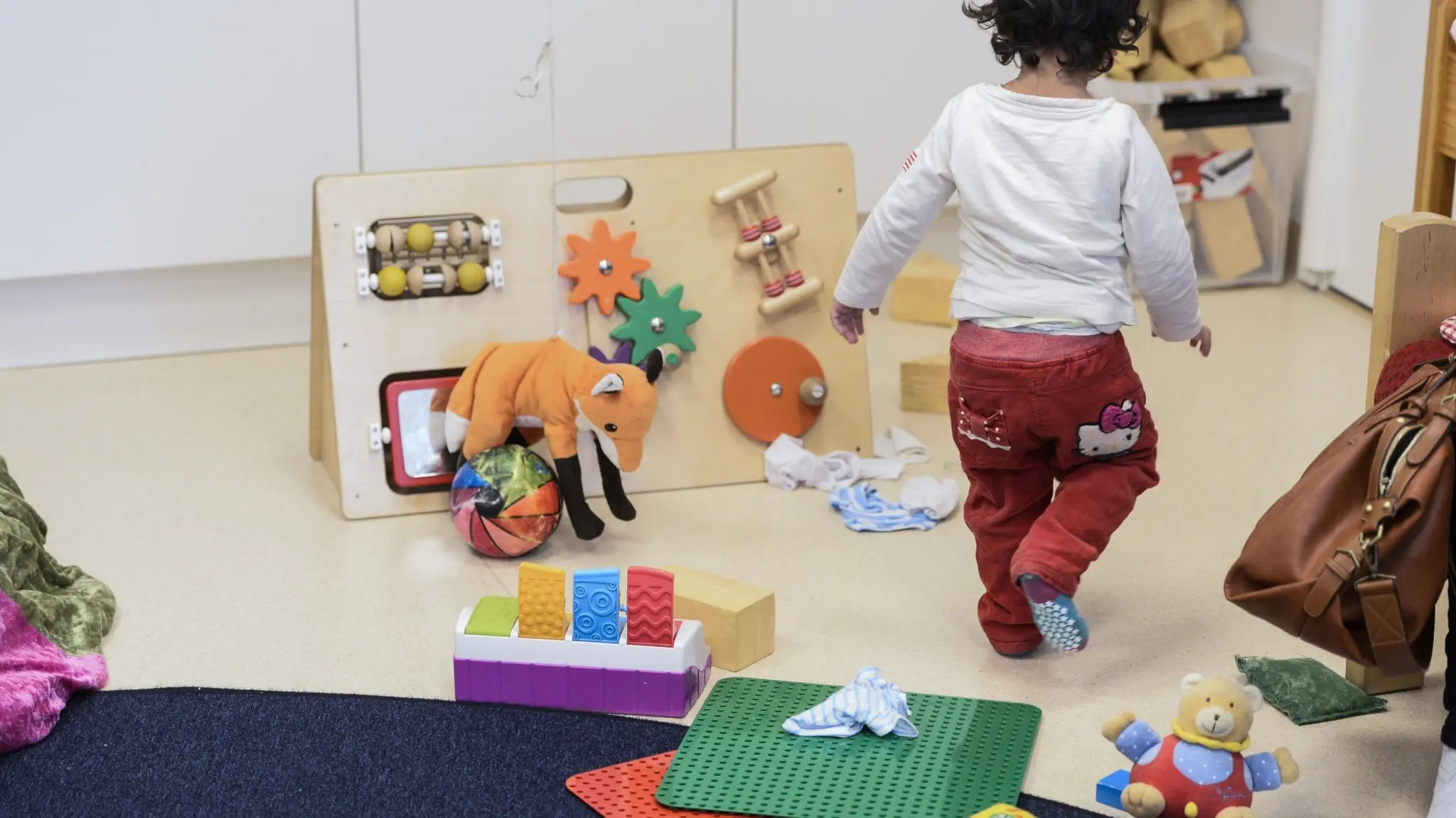 Ett barn leker på en förskola. Rummet är fyllt med färgglada leksaker och pedagogiska material. 