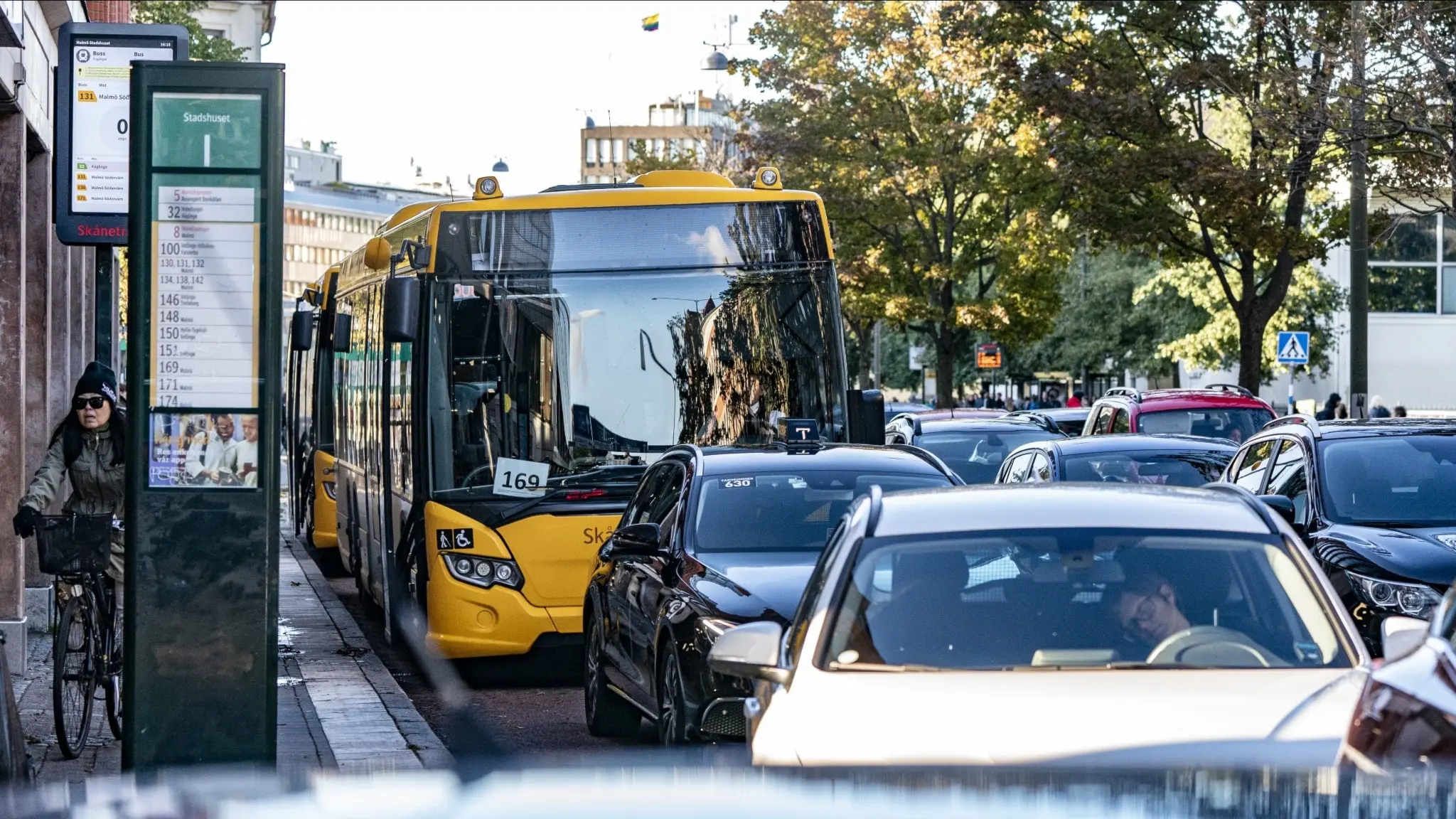 Bild av en gul buss. Runtomkring bussen ses flera personbilar. 
