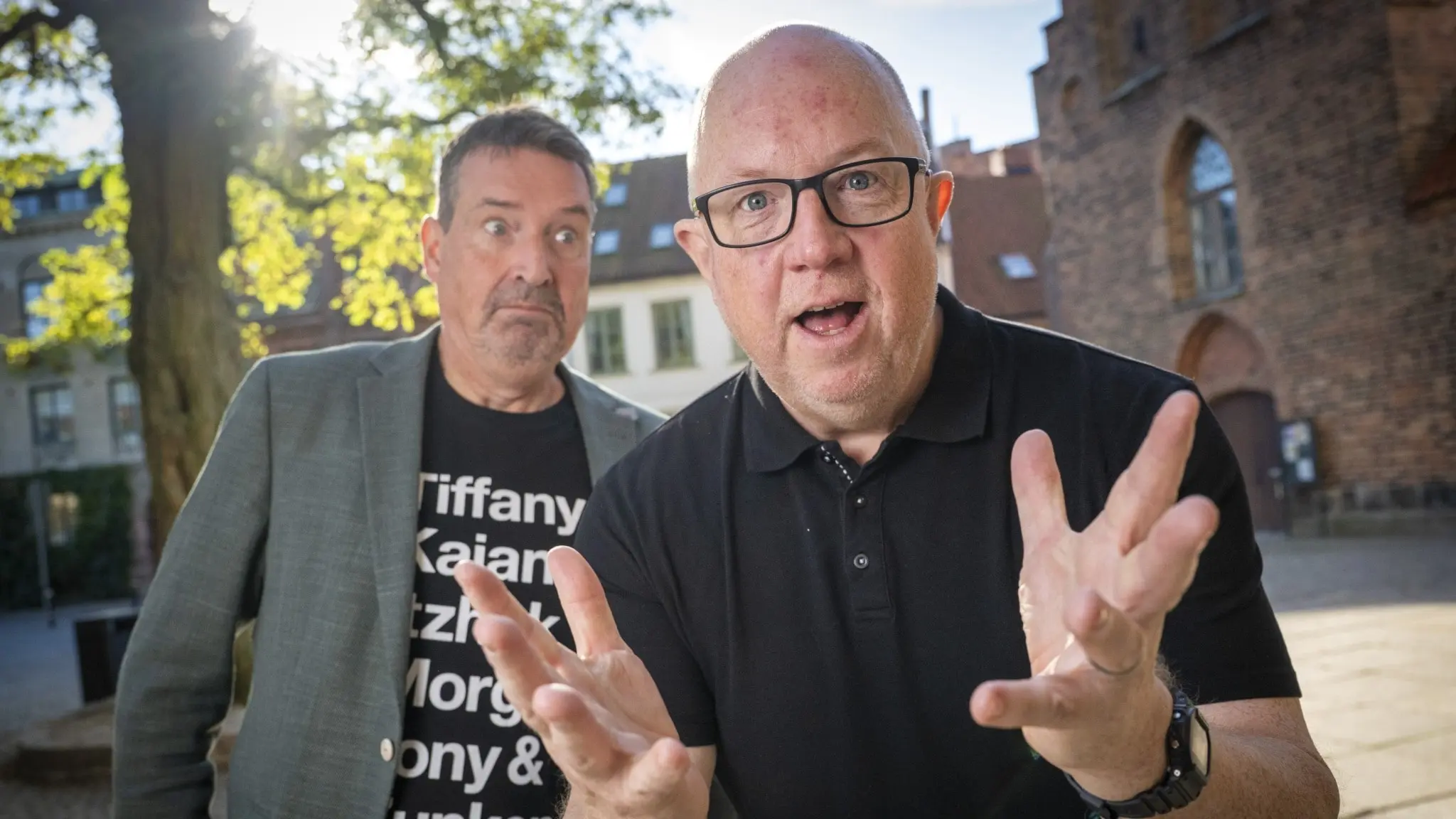 Johan Wester och Anders Jansson, kända från humorserien "Hipp Hipp", står utomhus framför en kyrka i soligt väder. Wester bär en grå kavaj och Jansson en svart tröja med vit text.