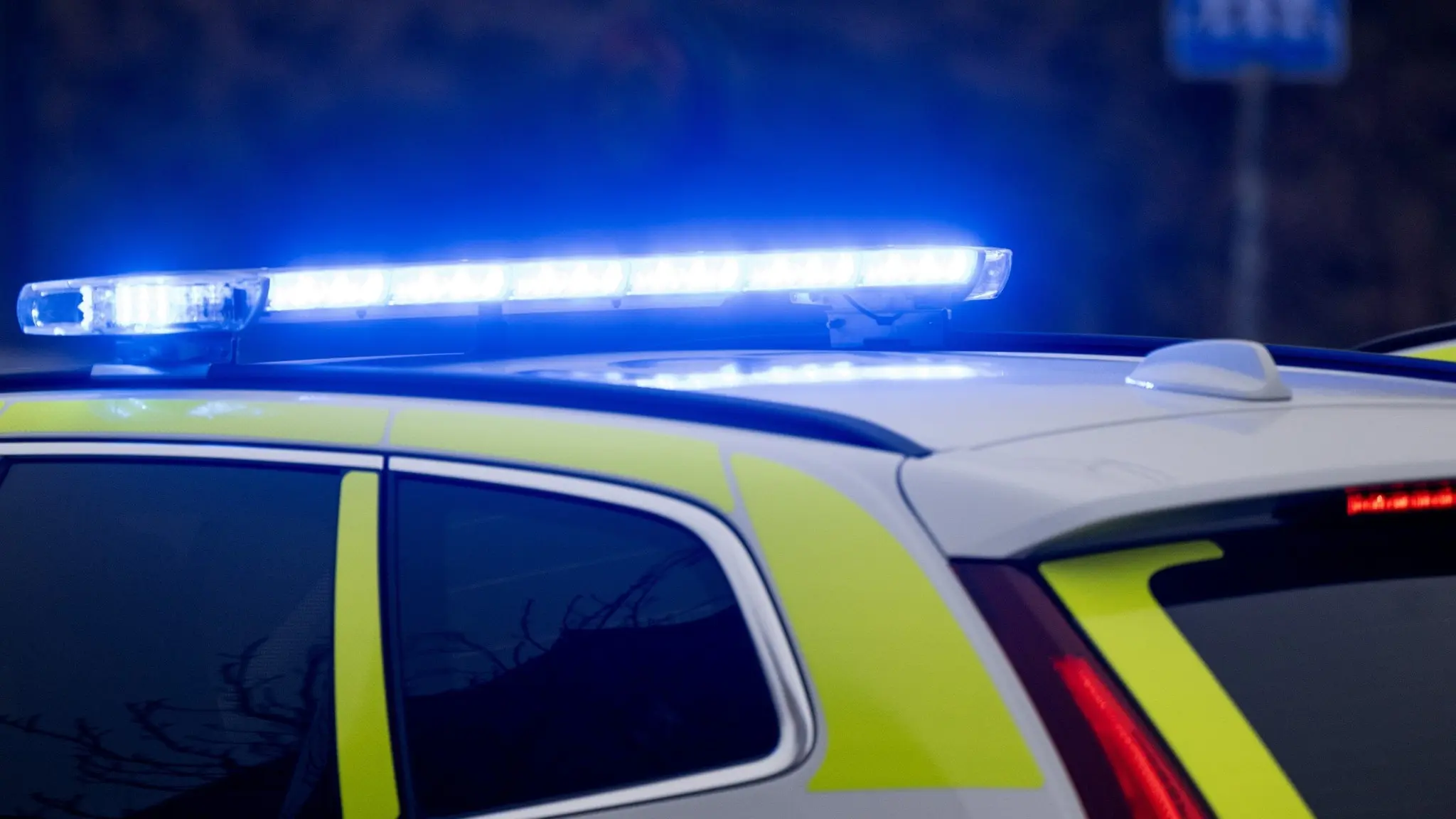 Polisbil med blåljus på taket, parkerad nära en övergångsskylt. Bilden symboliserar ett pågående polisärende där ett barn ska ha blivit hotat med kniv av en okänd gärningsman.