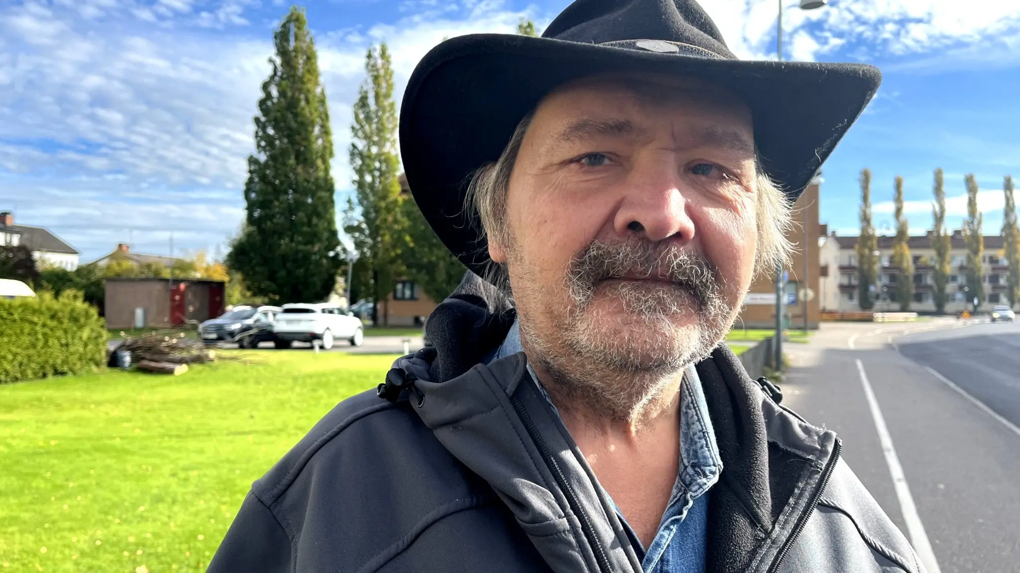 En man med hatt står utmed en väg och en gräsmatta.