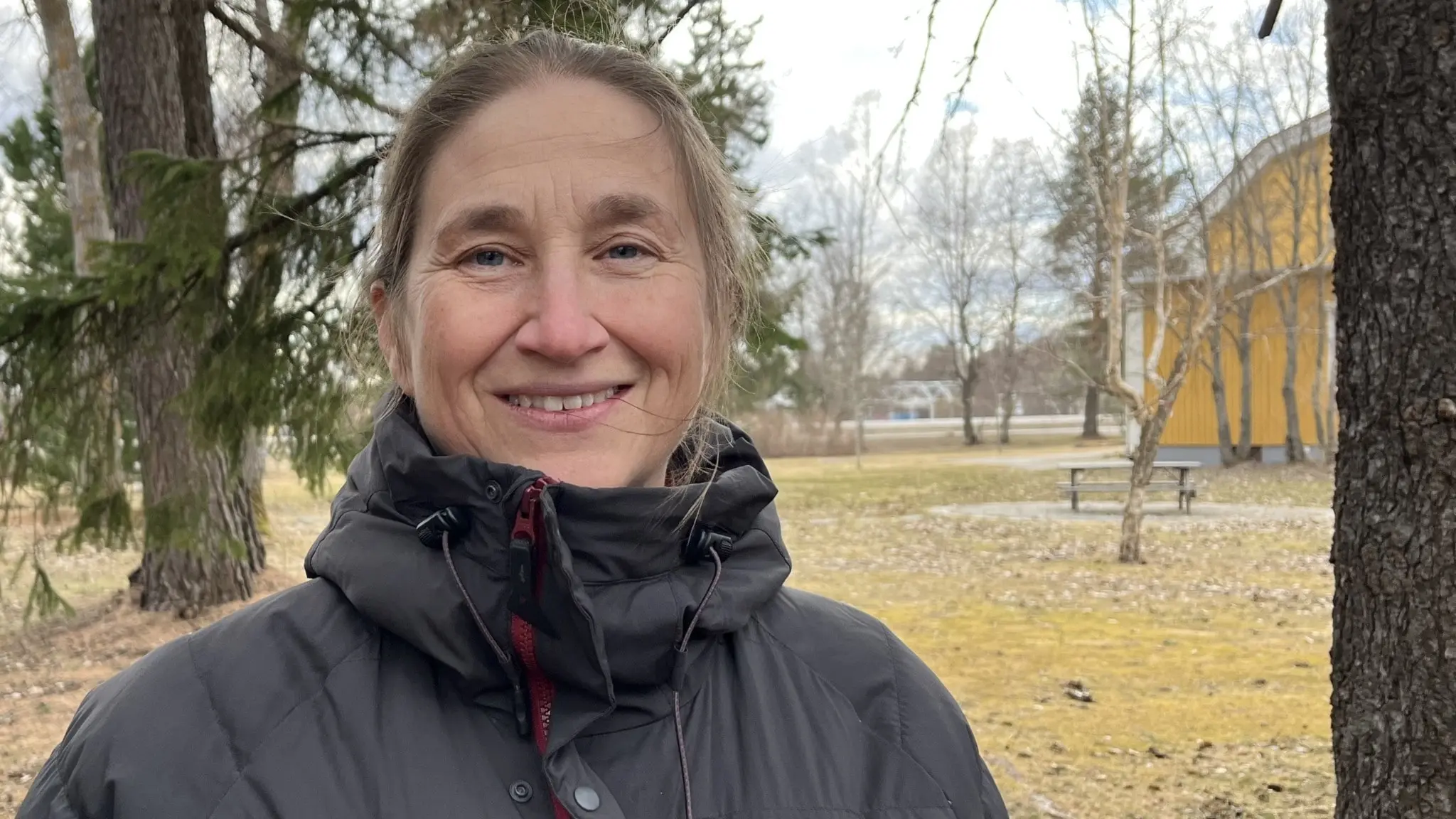 Marie Lundberg från Hushållningssällskapet står utomhus i en park med träd och en gul byggnad i bakgrunden. Hon diskuterar möjligheten att odla vete i Norrbotten.