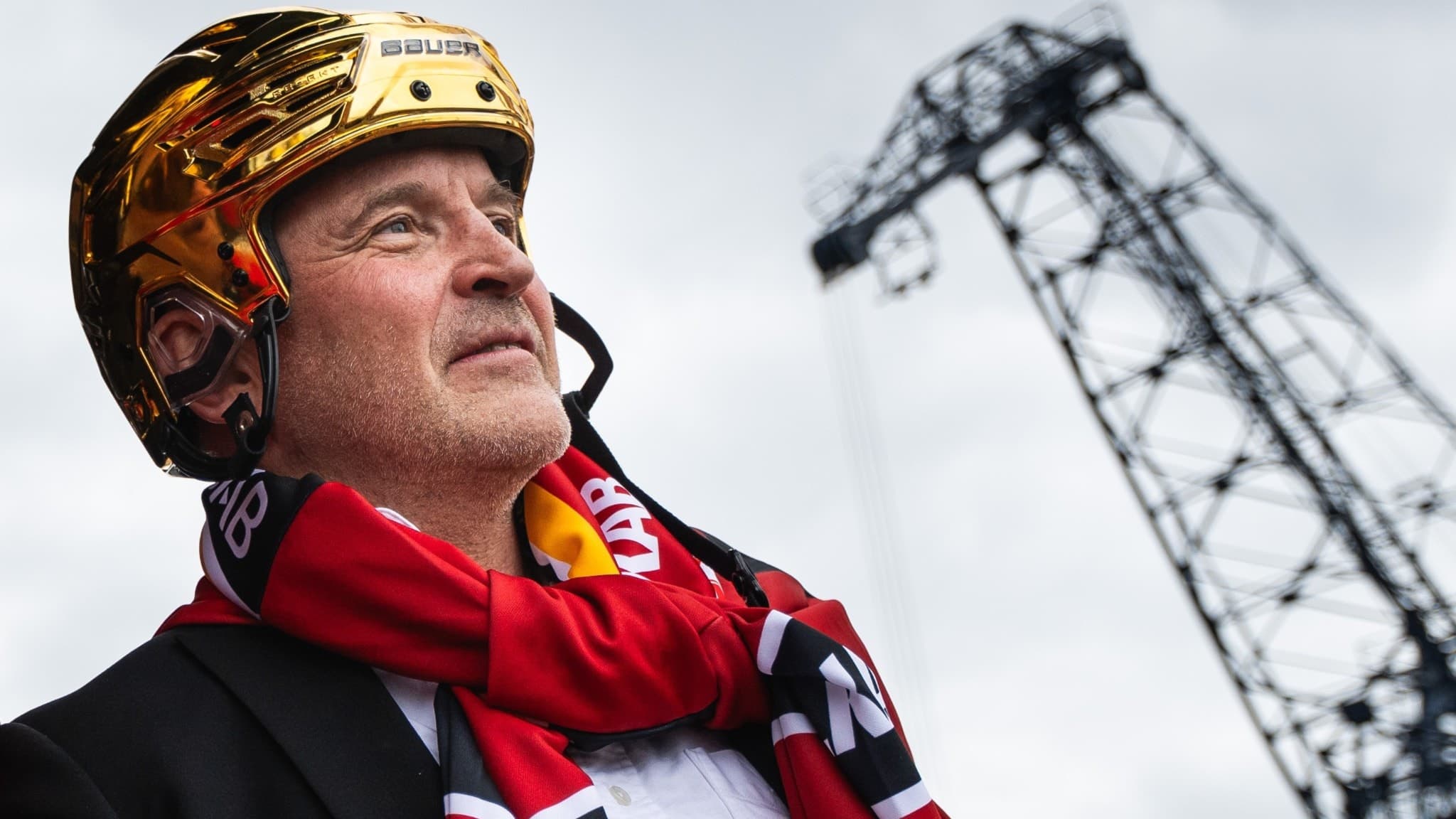 Luleå Hockeys tränare Thomas Berglund bär guldhjälm och röd halsduk under firandet av SM-guldet vid Södra hamn, med en kran i bakgrunden mot molnig himmel.