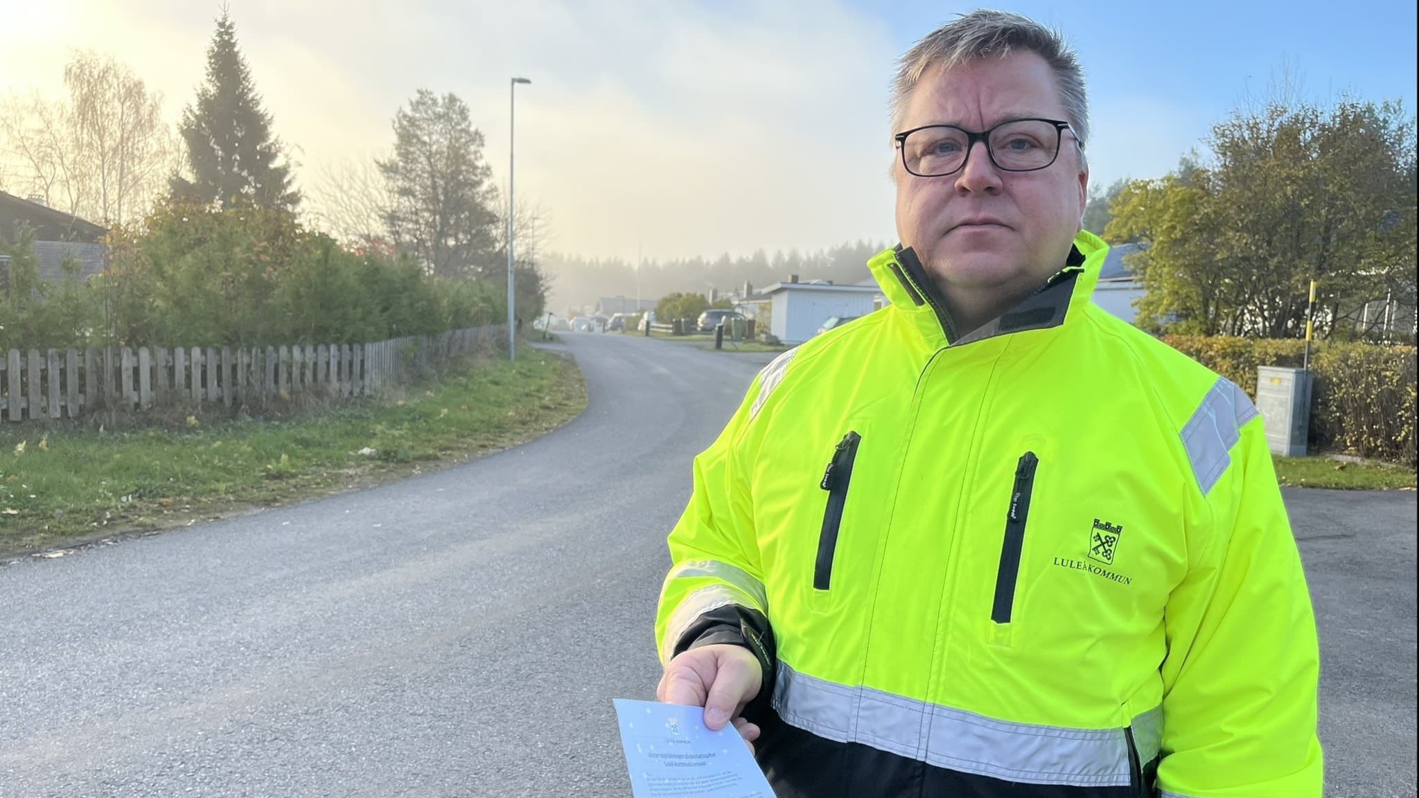 Patrik Ruumensaari, gatuchef i Luleå, står utomhus i en gul reflexjacka och håller ett brev riktat till villaägare, i bakgrunden syns  villor och en skogsdunge.