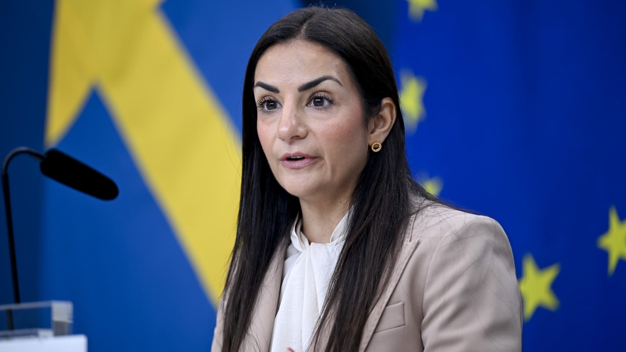 Kulturminister Parisa Liljestrand (M) står vid ett podium under en pressträff, med svenska flaggan och EU-flaggan i bakgrunden, för att presentera kulturdepartementets delar av höstbudgeten.