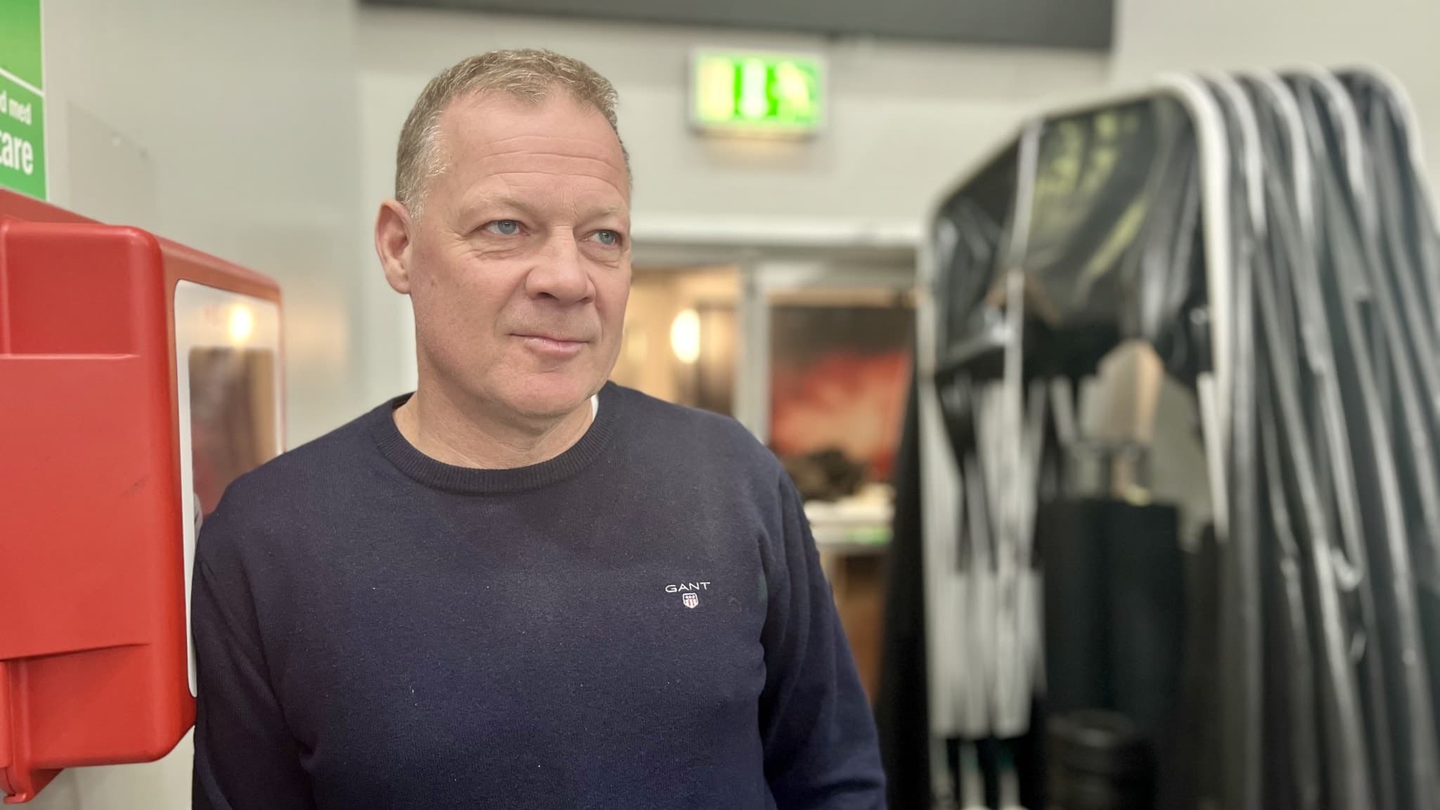 Henrik Stridh, Luleå Hockeys assisterande tränare, står inomhus vid ställ med hockeyklubbor och en brandsläckare. 