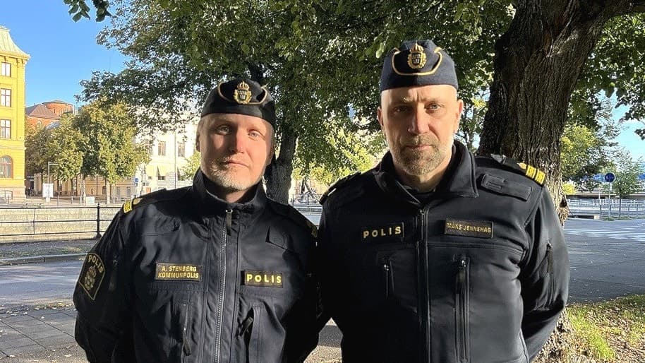 Poliserna Anders Stenberg och Måns Jennehag är klädda i uniform och står utomhus i en park i Gävle träd i bakgrunden. Solen skiner och det är en klar dag.