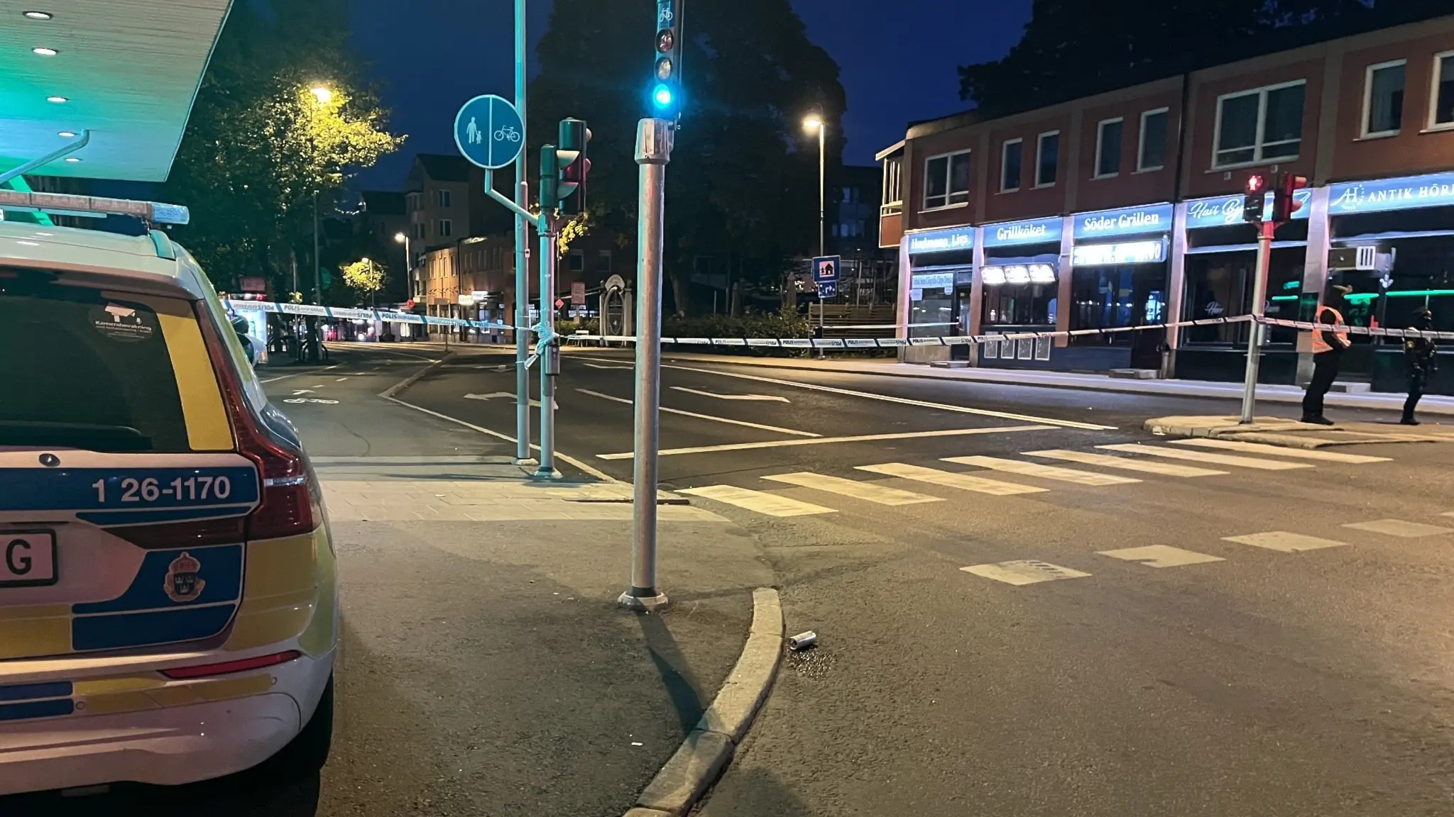 En polisbil står vid en avspärrad gata i centrala Gävle efter en skottlossning. Området är upplyst av gatlampor och flera byggnader syns i bakgrunden.