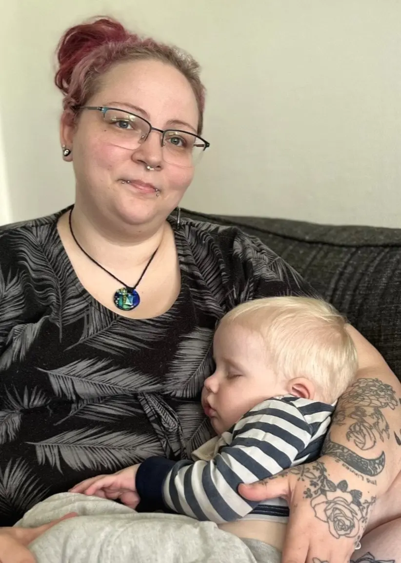 Natalie Backlund i Olofström sitter i en soffa med sin sovande som i famnen. 