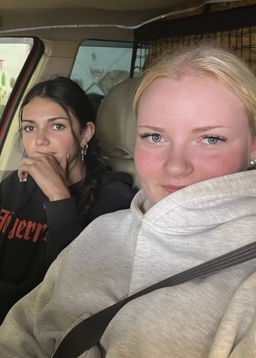 Alice Wallander och Julia Ågren sitter i en bil. Bilden visar interiören av bilen med två personer i förarsätet och passagerarsätet. Bakgrunden inkluderar en färgglad väggmålning utanför bilen.