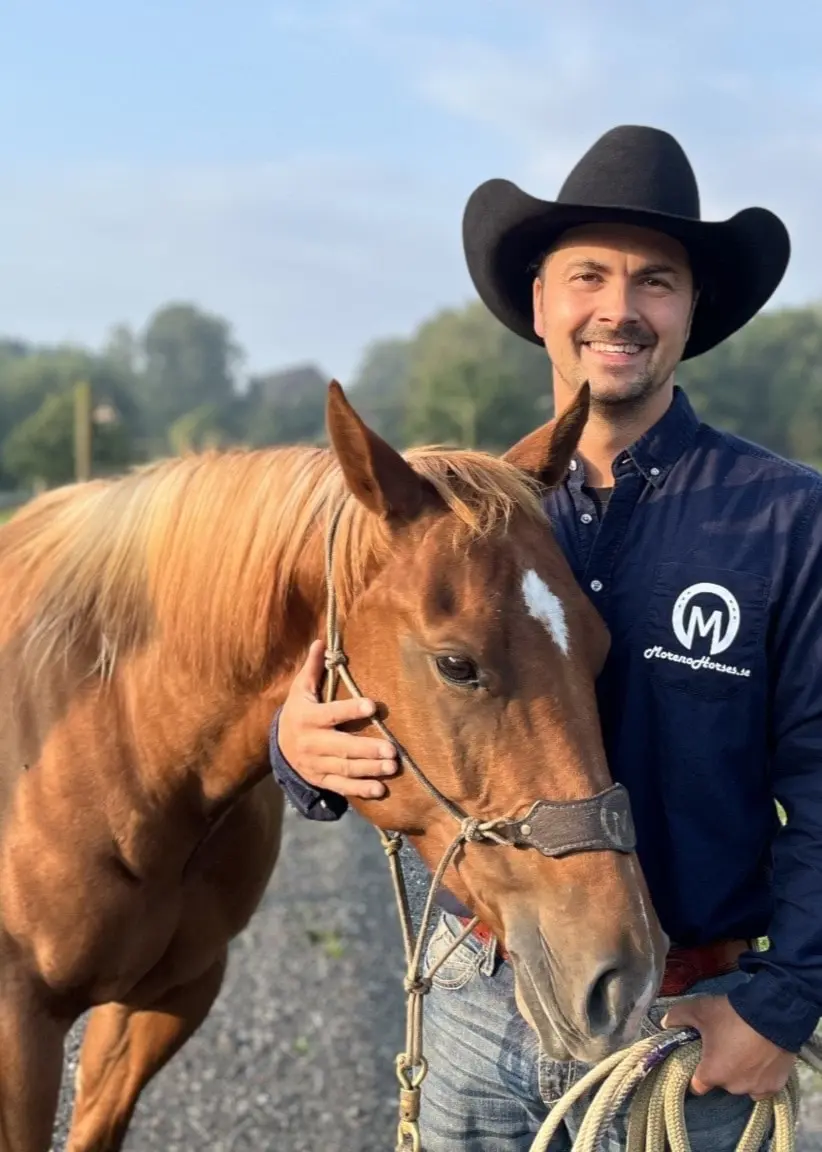 Man i cowboyhatt, står med en häst framför en hage